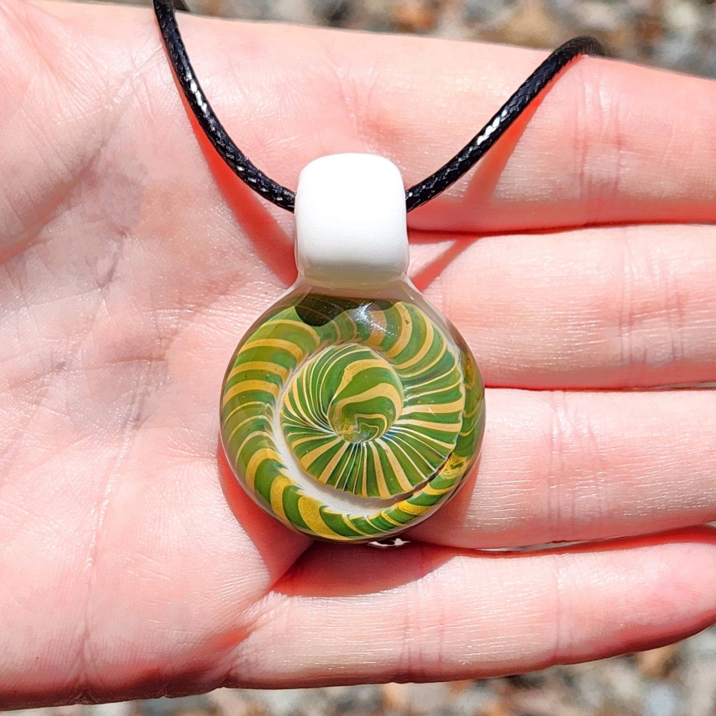 Front view of Handmade Spiral Glass Pendant held in hand, highlighting vibrant green-yellow spiral and smooth white glass top.