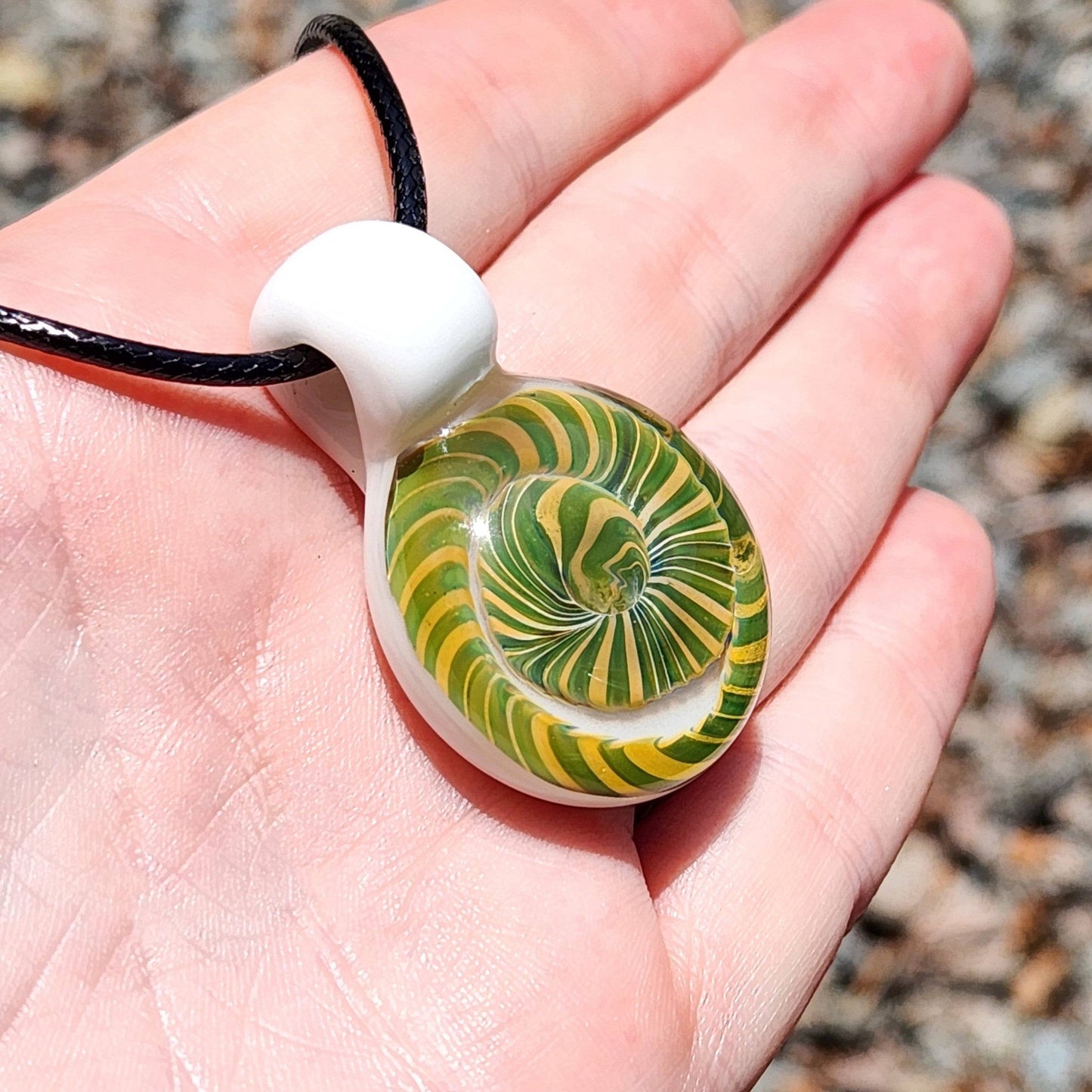 Handmade Spiral Glass Pendant displayed in hand under sunlight, showing green-yellow spiral and white loop for scale and detail.