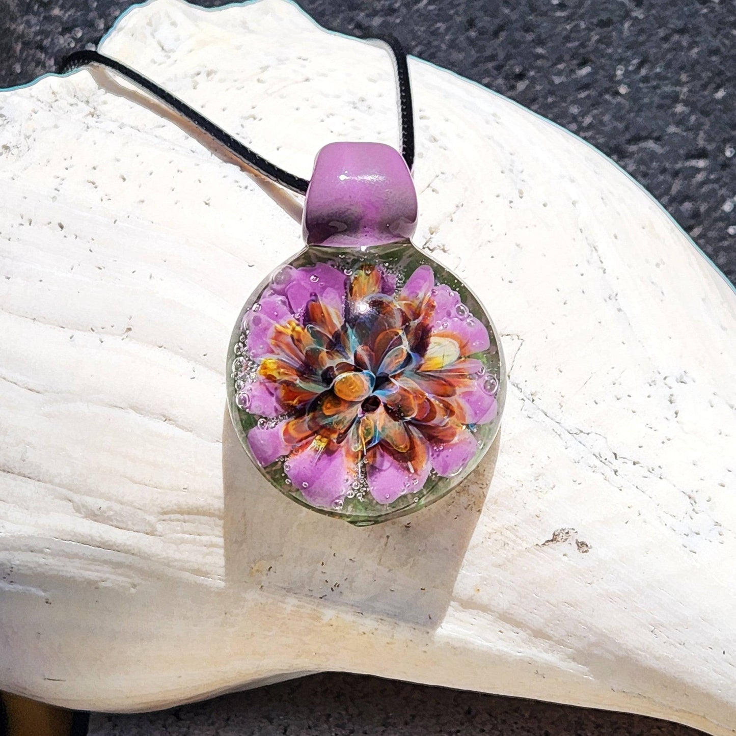 Handmade multicolor glass pendant with purple, green, and orange flower design on black cord. Borosilicate jewelry for unique necklace styles.