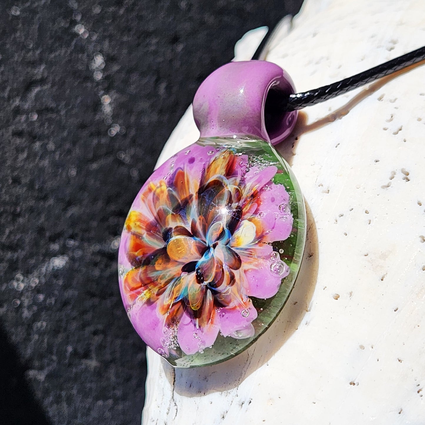 Detailed side angle of multicolor heady glass pendant with vibrant flower encased in clear dome. Handmade borosilicate necklace piece.