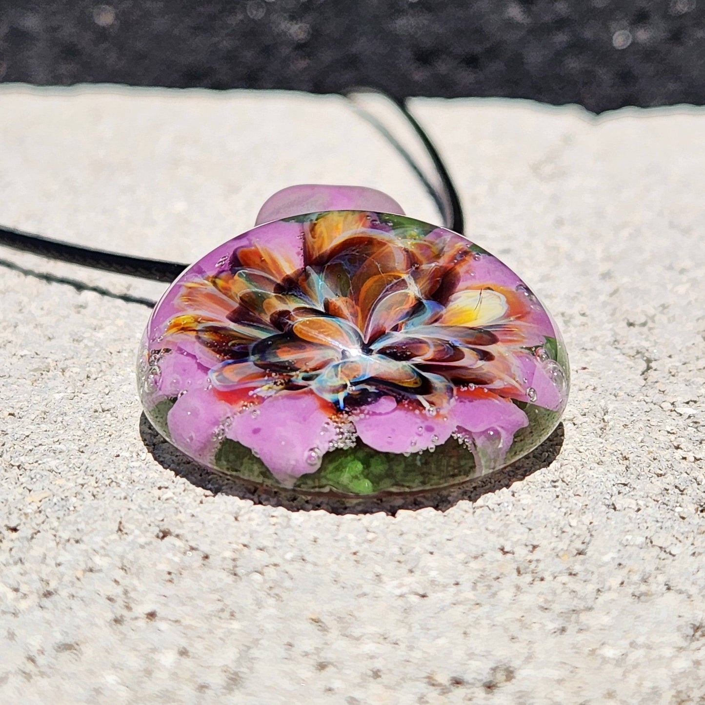Front view of handmade borosilicate pendant with layered flower in purple, orange, and green. Artistic glass necklace for gifting.