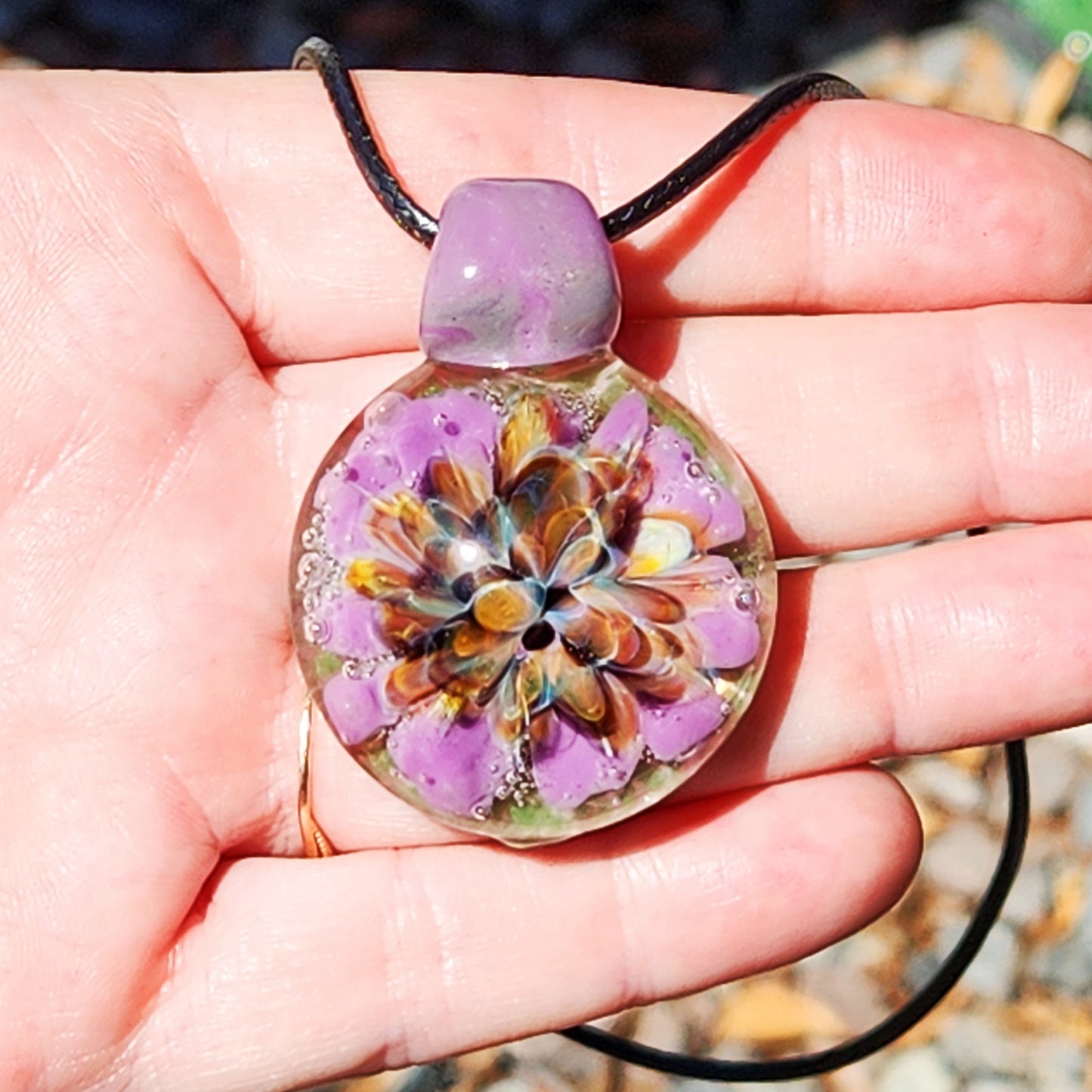 Hand holding handmade multicolor glass pendant with vibrant flower design. Borosilicate necklace for unique jewelry lovers.