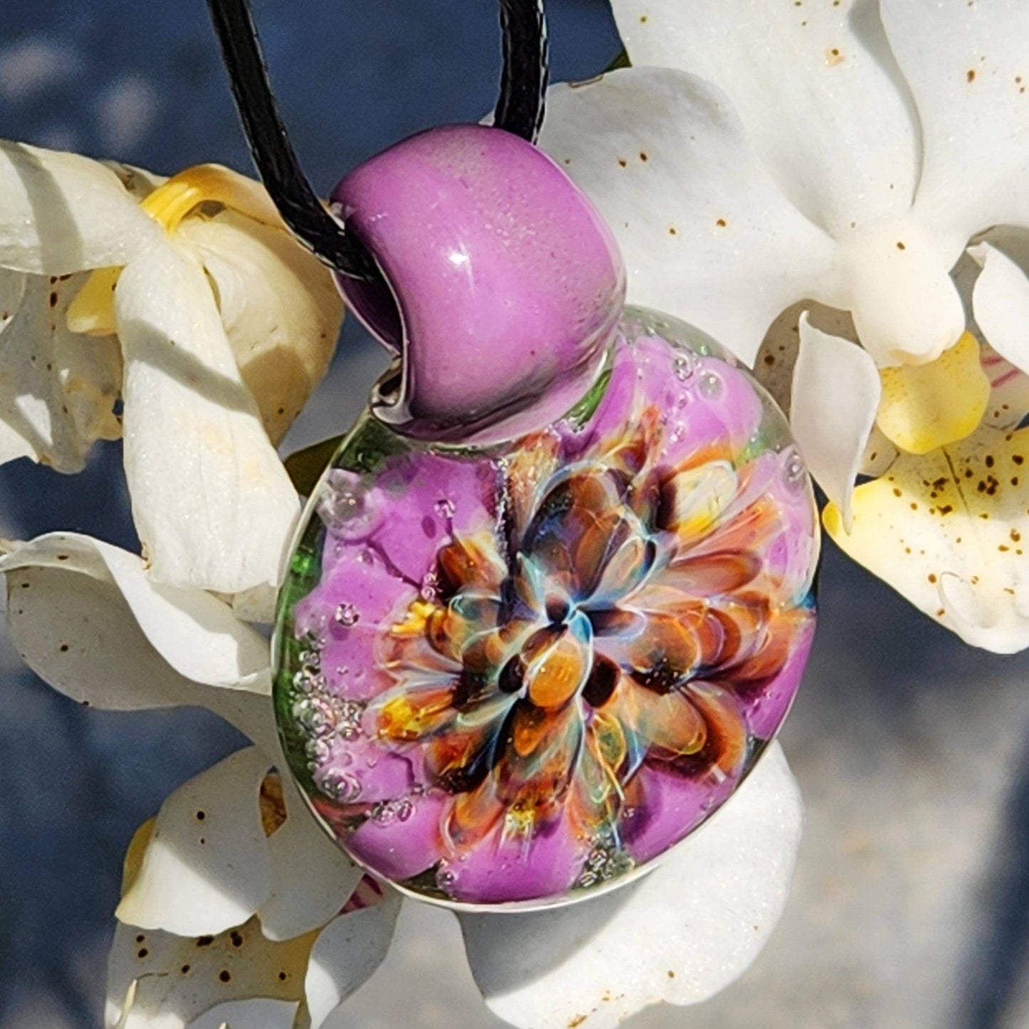 Close-up of handmade borosilicate glass pendant featuring vibrant flower pattern in purple, orange, and green tones. Heady glass necklace gift.