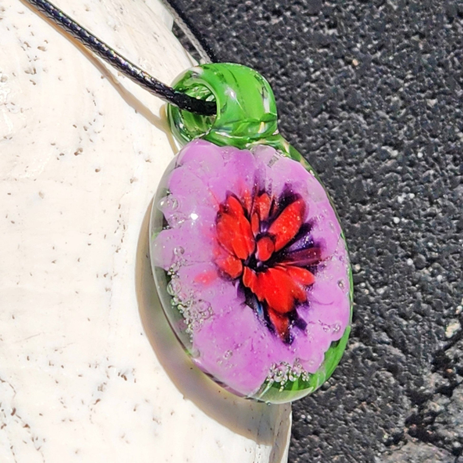 Side view of handmade blown glass pendant necklace with vibrant red and purple flower in green glass. Unique borosilicate jewelry for men or women.