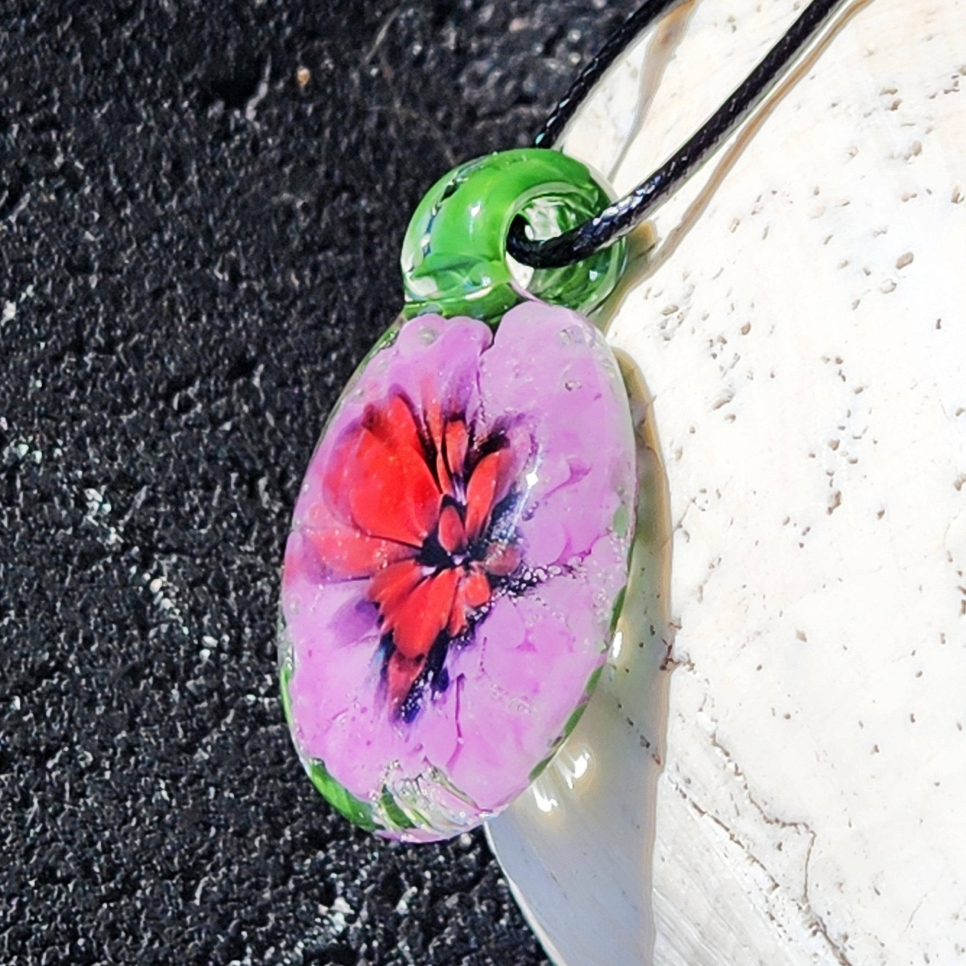 Detailed view of handmade glass pendant with red and purple flower encased in green. Unique blown glass jewelry art necklace for gifting.