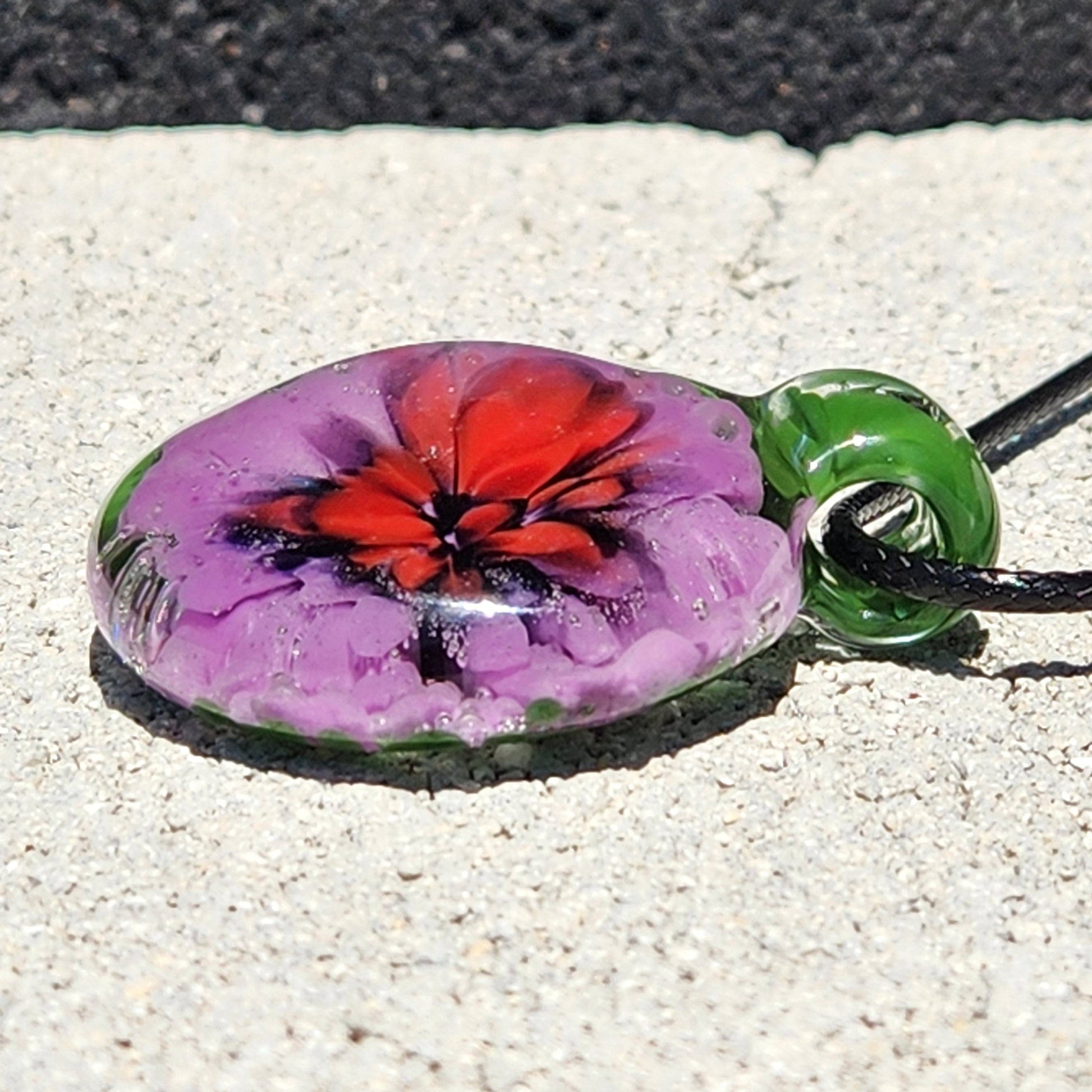 Close-up of Large Heady Glass Pendant Necklace showing red and purple floral swirl in green glass. Artistic handmade jewelry with a glossy finish.