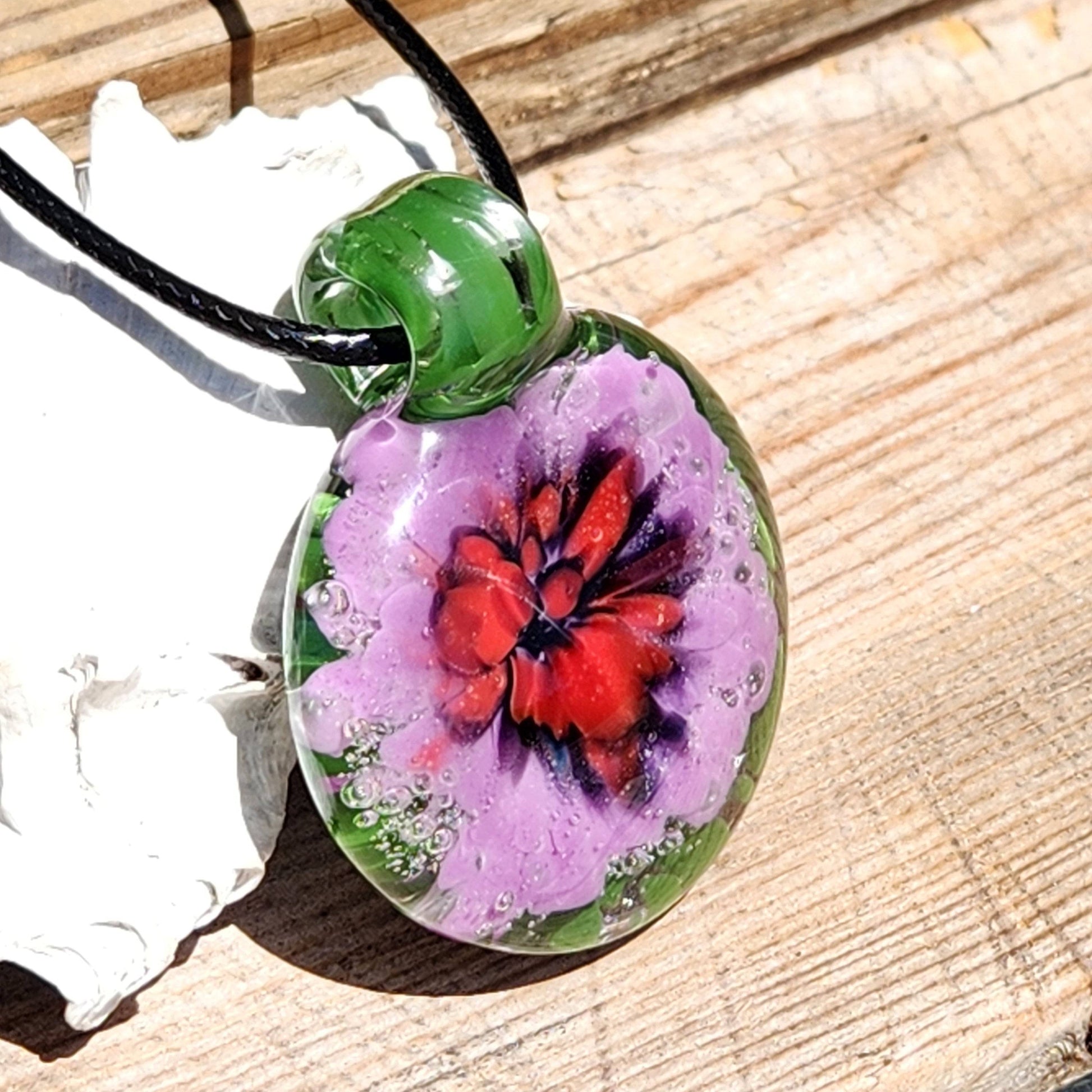 Handmade blown glass pendant with vivid red and purple flower on green background. Unique borosilicate jewelry art necklace for gifts or personal wear.