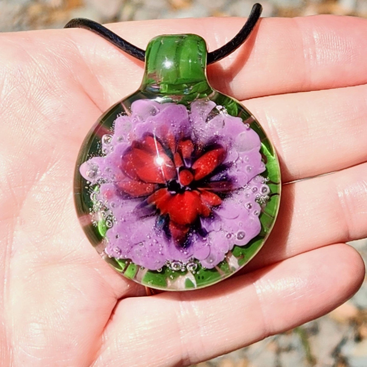 Large Heady Glass Pendant Necklace displayed in hand, highlighting red and purple flower in green glass. Handmade borosilicate jewelry art piece.