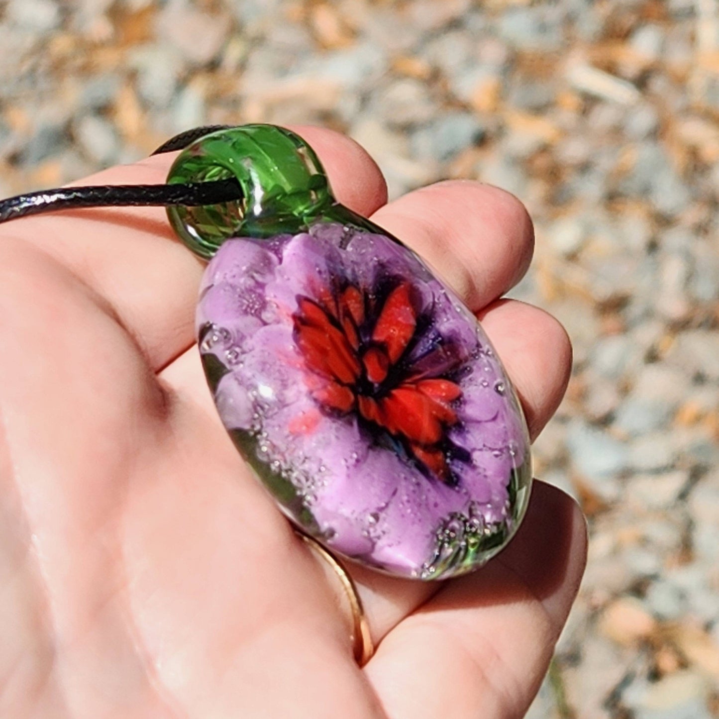 Hand holding Large Heady Glass Pendant Necklace with red and purple flower in green glass. Unique handmade jewelry art for everyday wear.