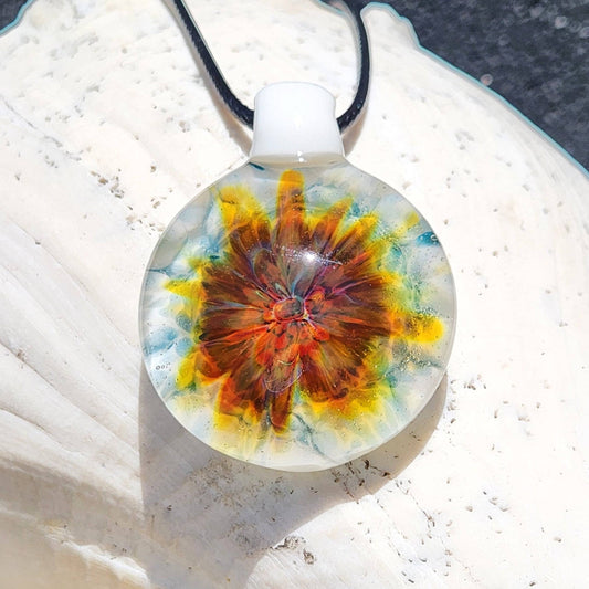 Unique lampworked glass pendant featuring a vibrant flower-like swirl in red, orange, and blue on a white base. Handmade jewelry beauty in glass.