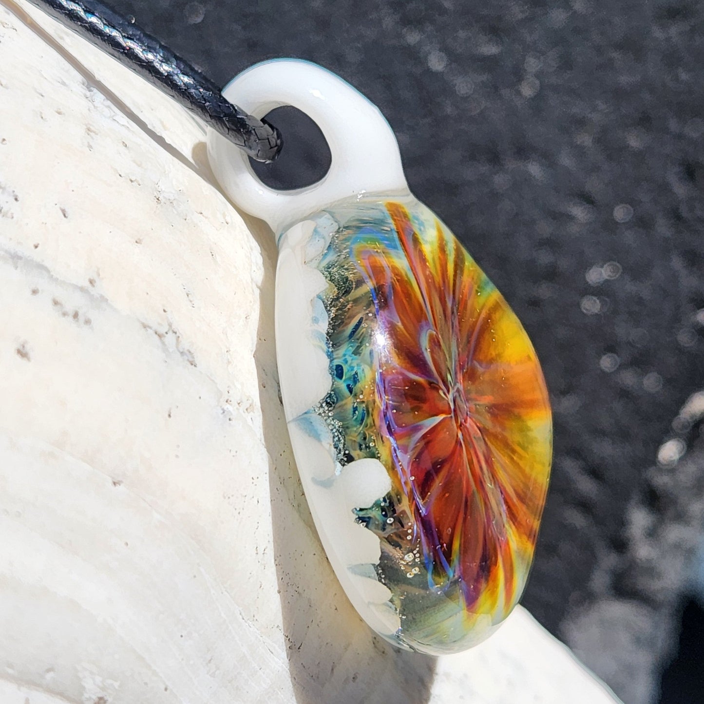 Side view of handmade blown glass pendant with colorful internal swirl and glossy white loop. Unique lampworked jewelry in borosilicate glass.