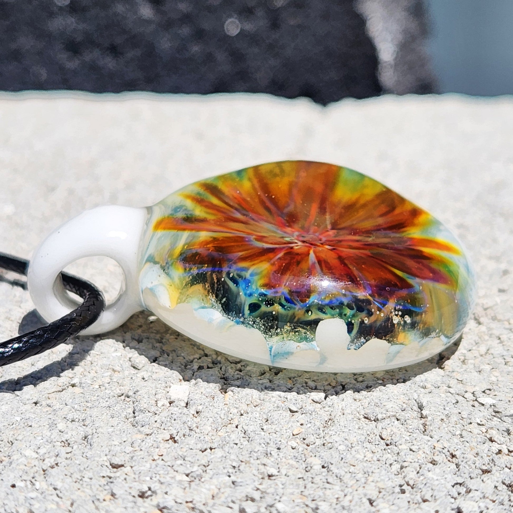 Artisan glass pendant resting on stone, showcasing fiery red and yellow swirls with a white base. Handmade jewelry beauty in glass.