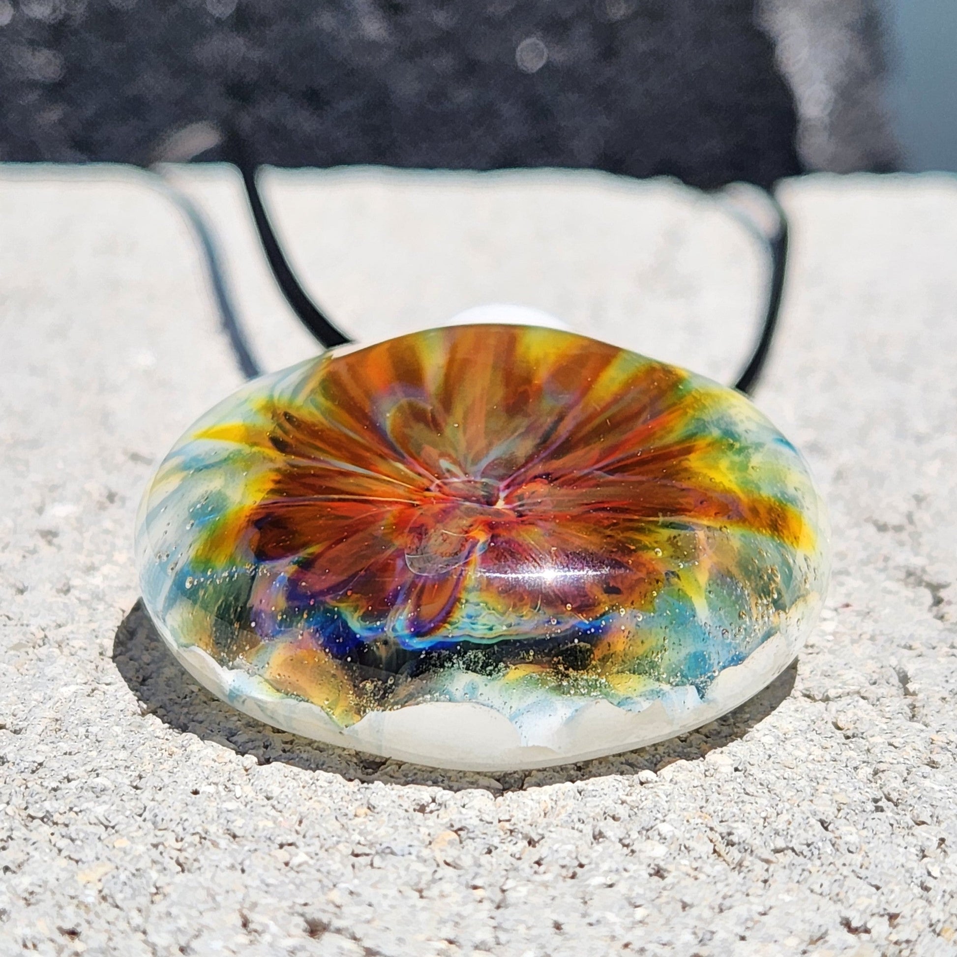 Colorful blown glass pendant with red, yellow, and blue swirls, set on a white base. Unique handmade jewelry beauty in borosilicate glass.