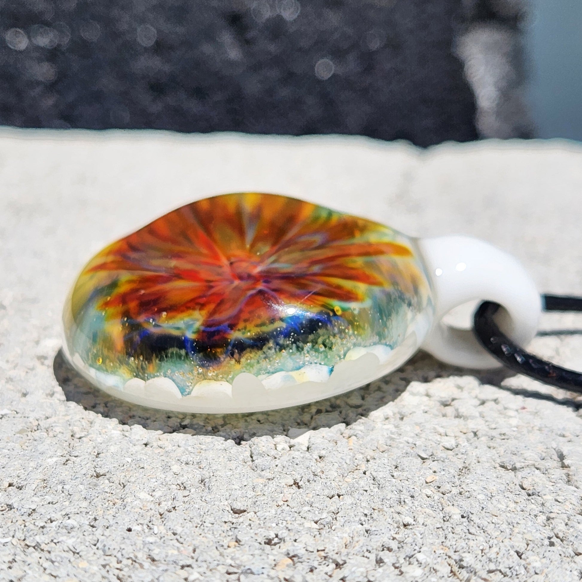 Angled view of blown glass pendant with vivid internal swirl and glossy finish. Unique handmade jewelry in borosilicate glass.