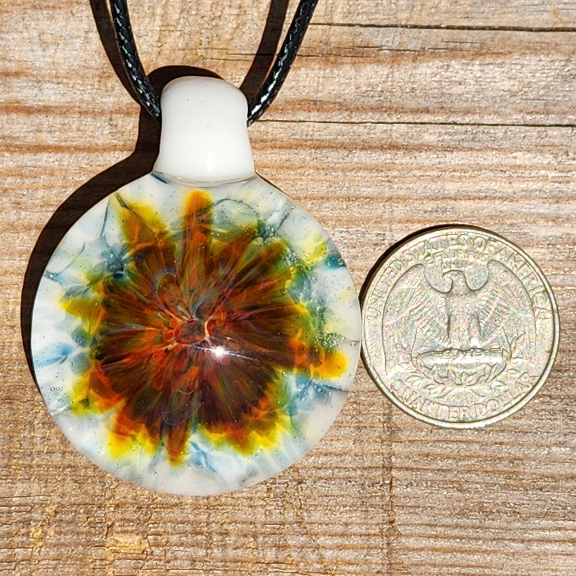Blown glass pendant next to a US quarter for size reference, featuring a colorful swirl on white. Unique handmade jewelry beauty in glass.