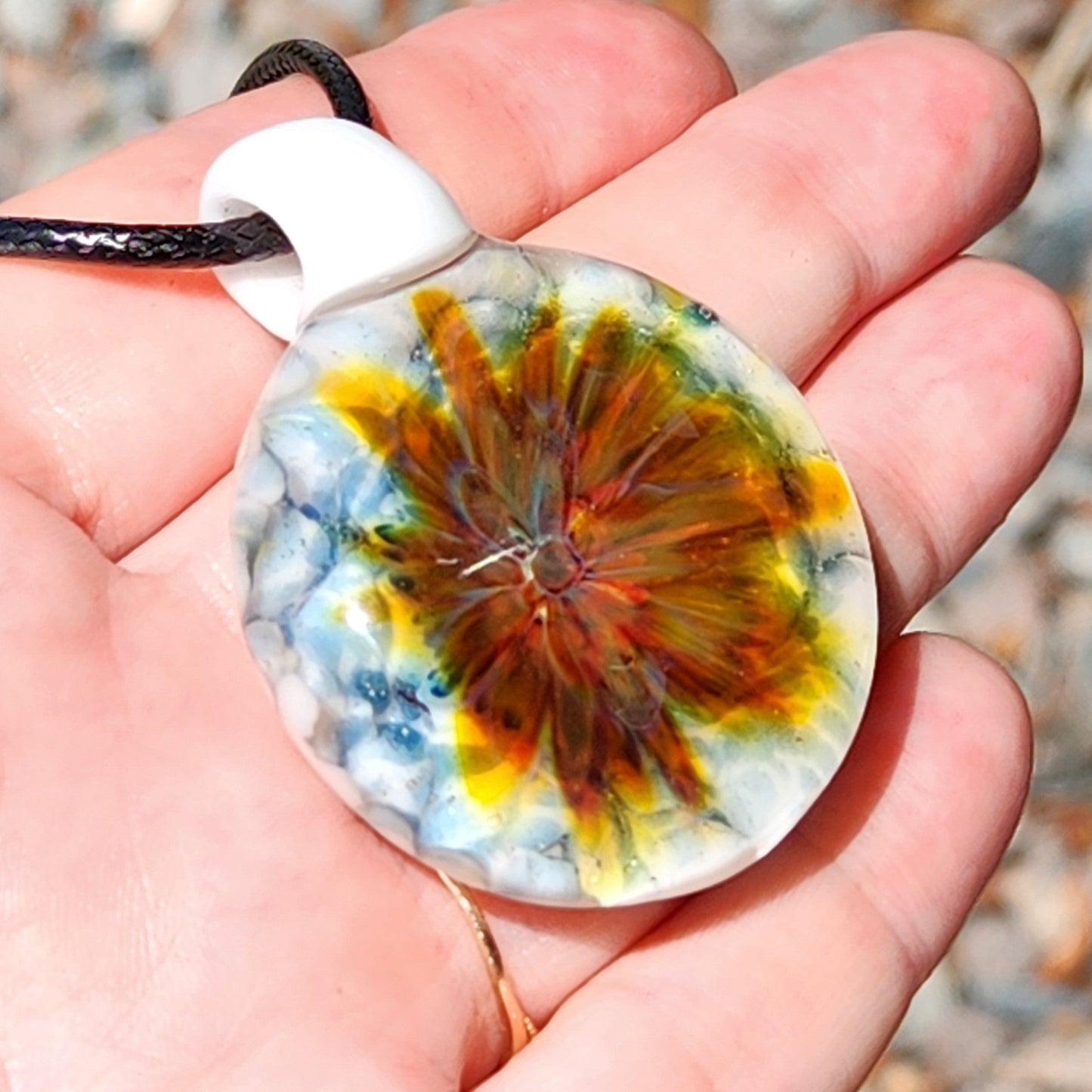Hand holding a unique lampworked glass pendant with vibrant floral design and white loop. Handmade jewelry beauty in glass craftsmanship.