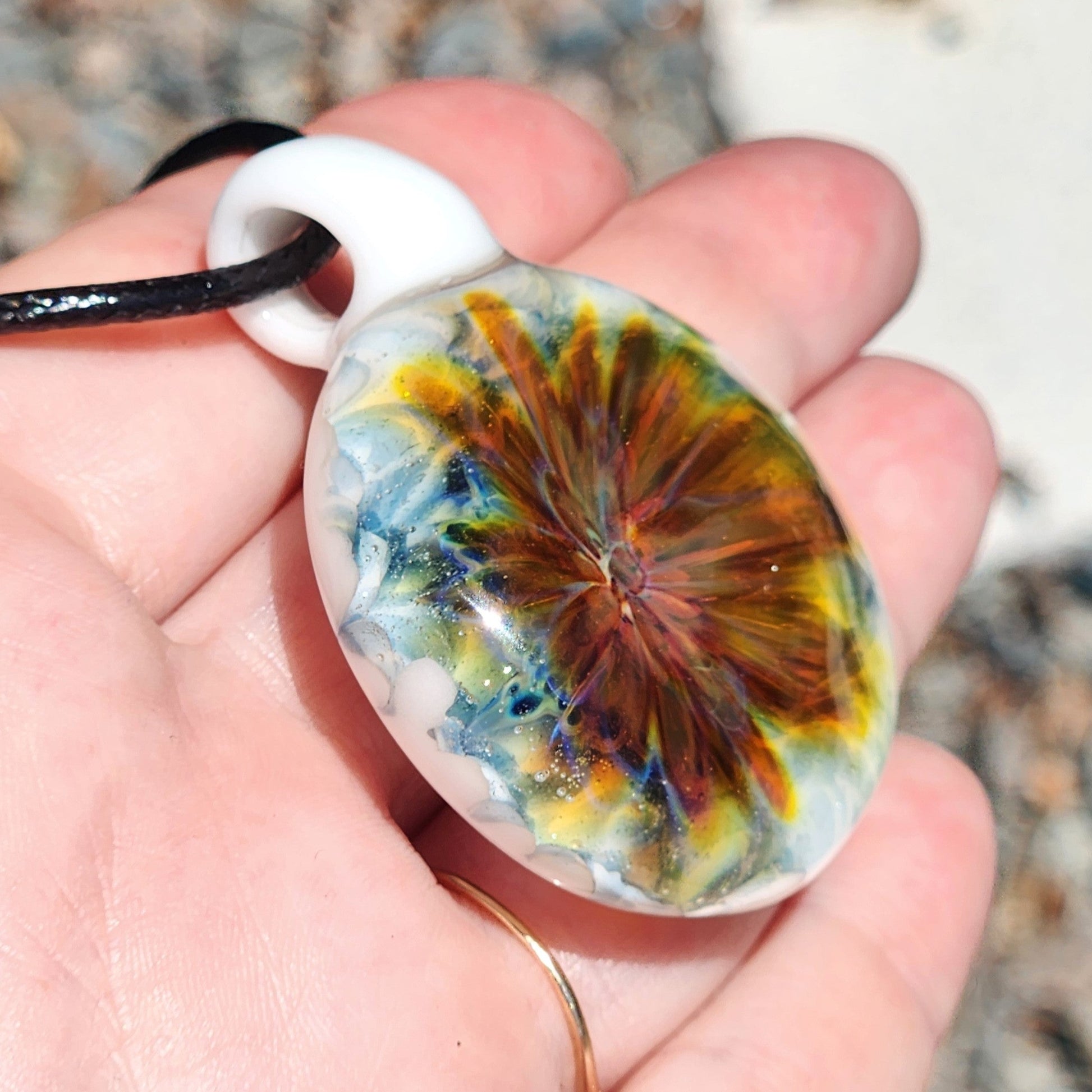 Hand displaying a vibrant handmade glass pendant with red and yellow swirl on white. Unique lampworked jewelry beauty in borosilicate glass.