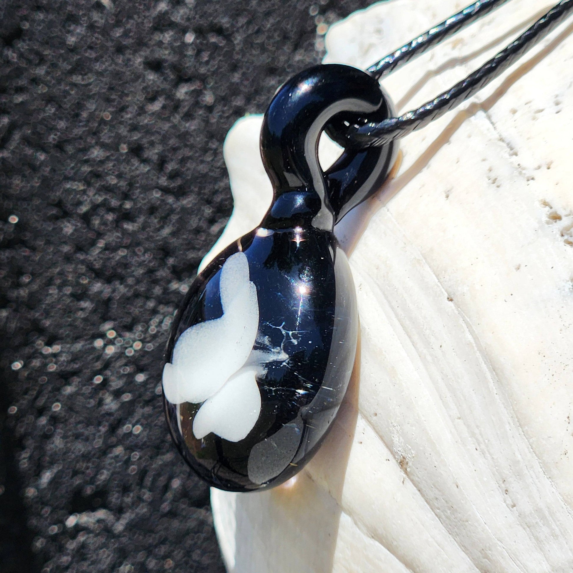 Angled view of handmade black and white glass pendant with butterfly design, showcasing its glossy finish and craftsmanship.