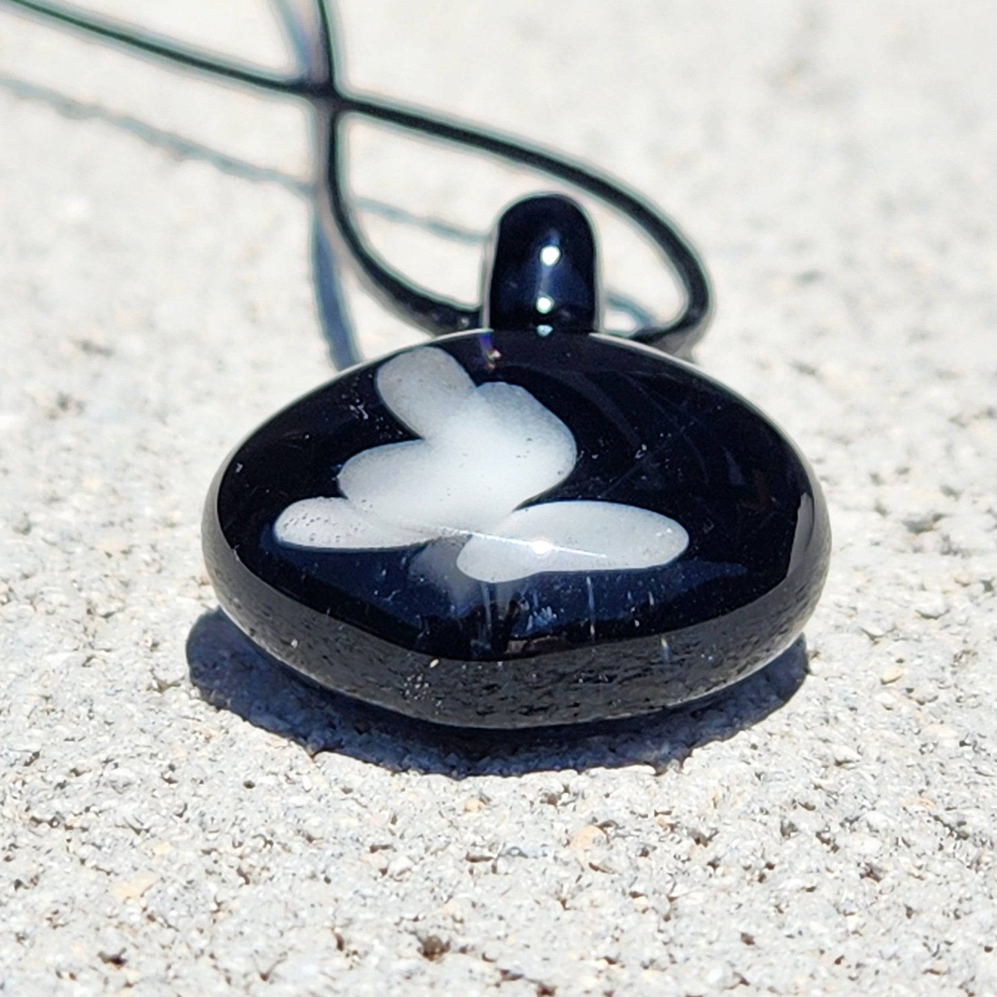 Flat view of small black glass pendant with white butterfly, a durable and stylish handmade accessory for everyday wear.
