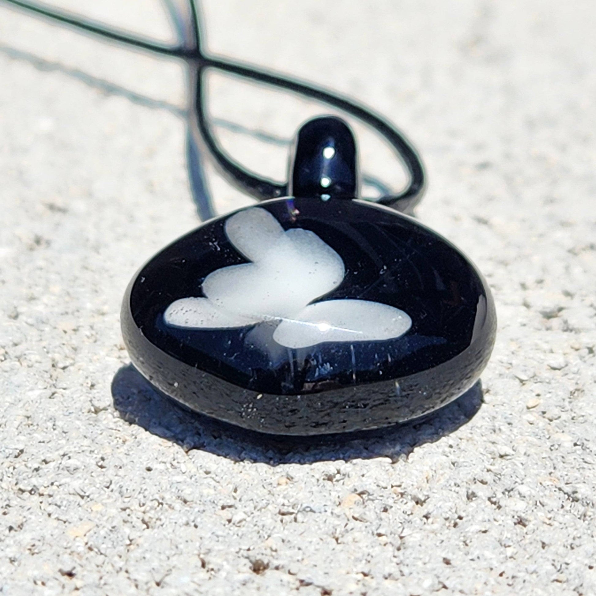 Flat view of small black glass pendant with white butterfly, a durable and stylish handmade accessory for everyday wear.