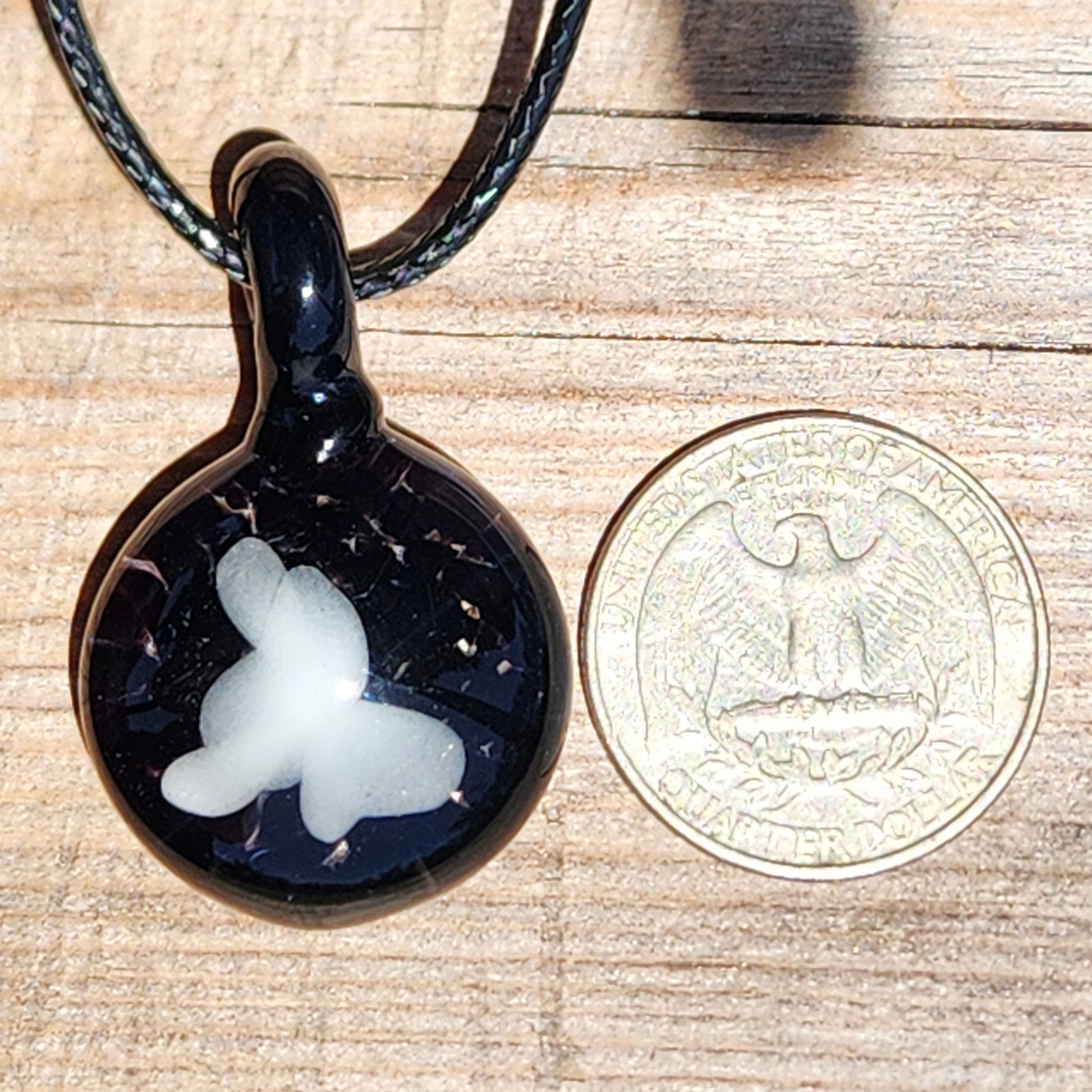 Size comparison of Small Black and White Glass Pendant next to a US quarter, showing its compact and wearable design.
