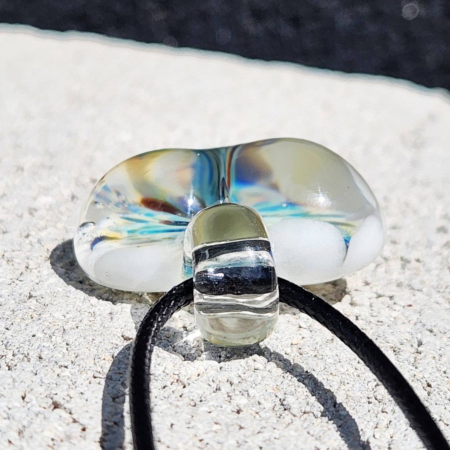 Bottom view of handmade blown glass heart pendant showing clear loop and colorful internal swirls, placed on a light stone surface.