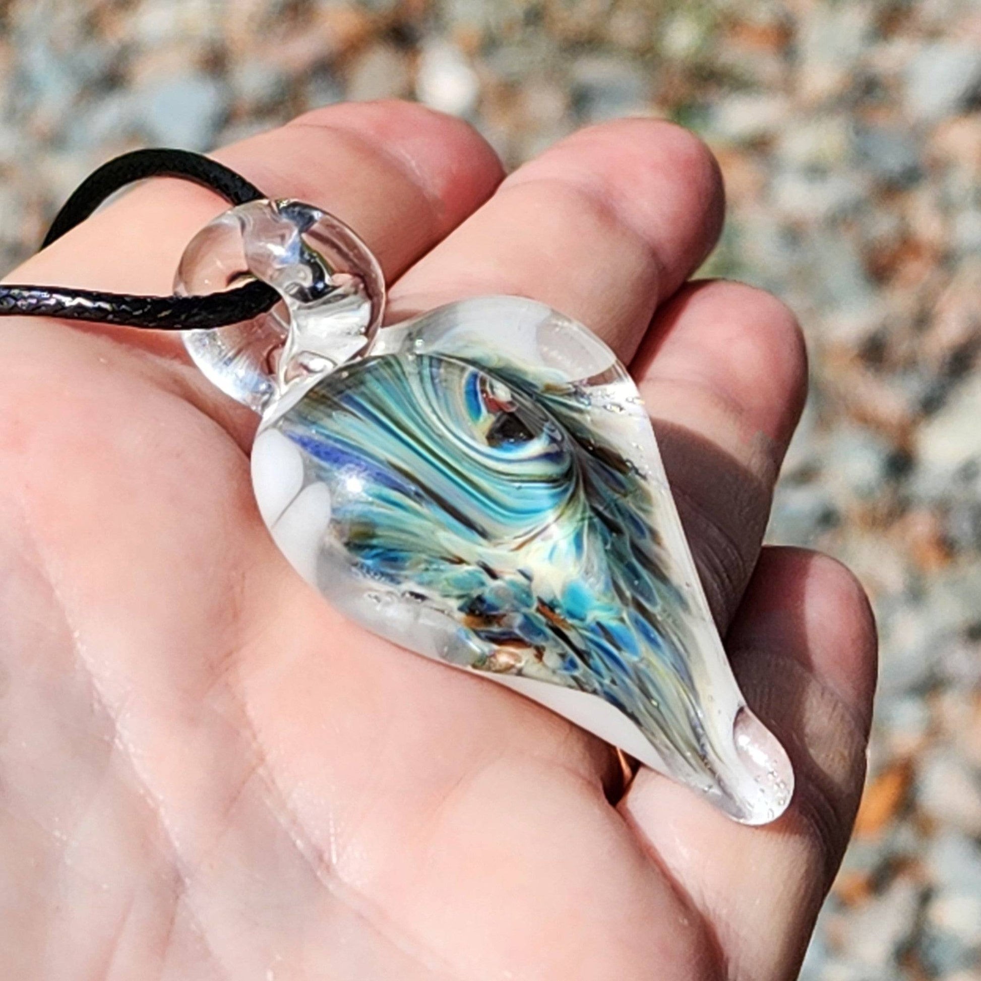 Side angle of heart-shaped handmade glass pendant with colorful implosion design, held in hand with outdoor background.