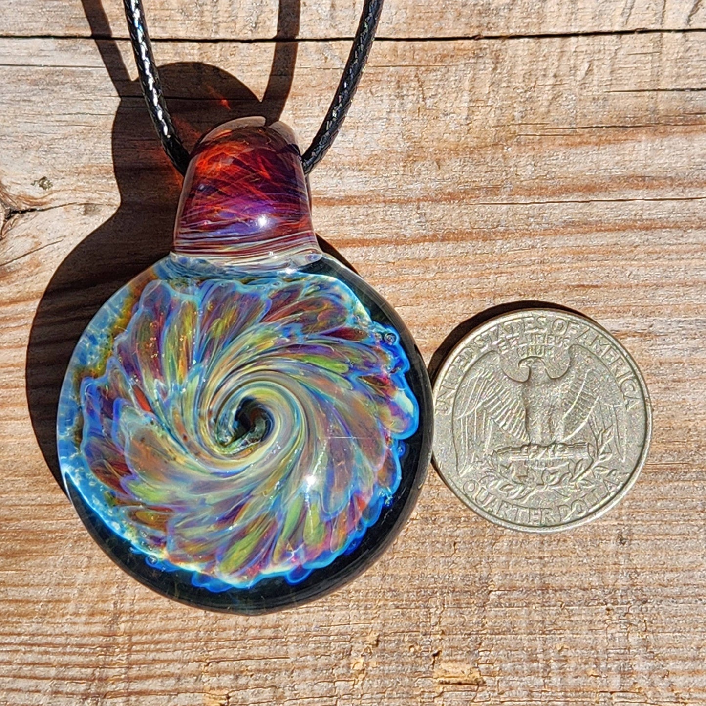 Size comparison of handmade multicolor glass pendant necklace next to a US quarter, showing detailed swirl pattern.