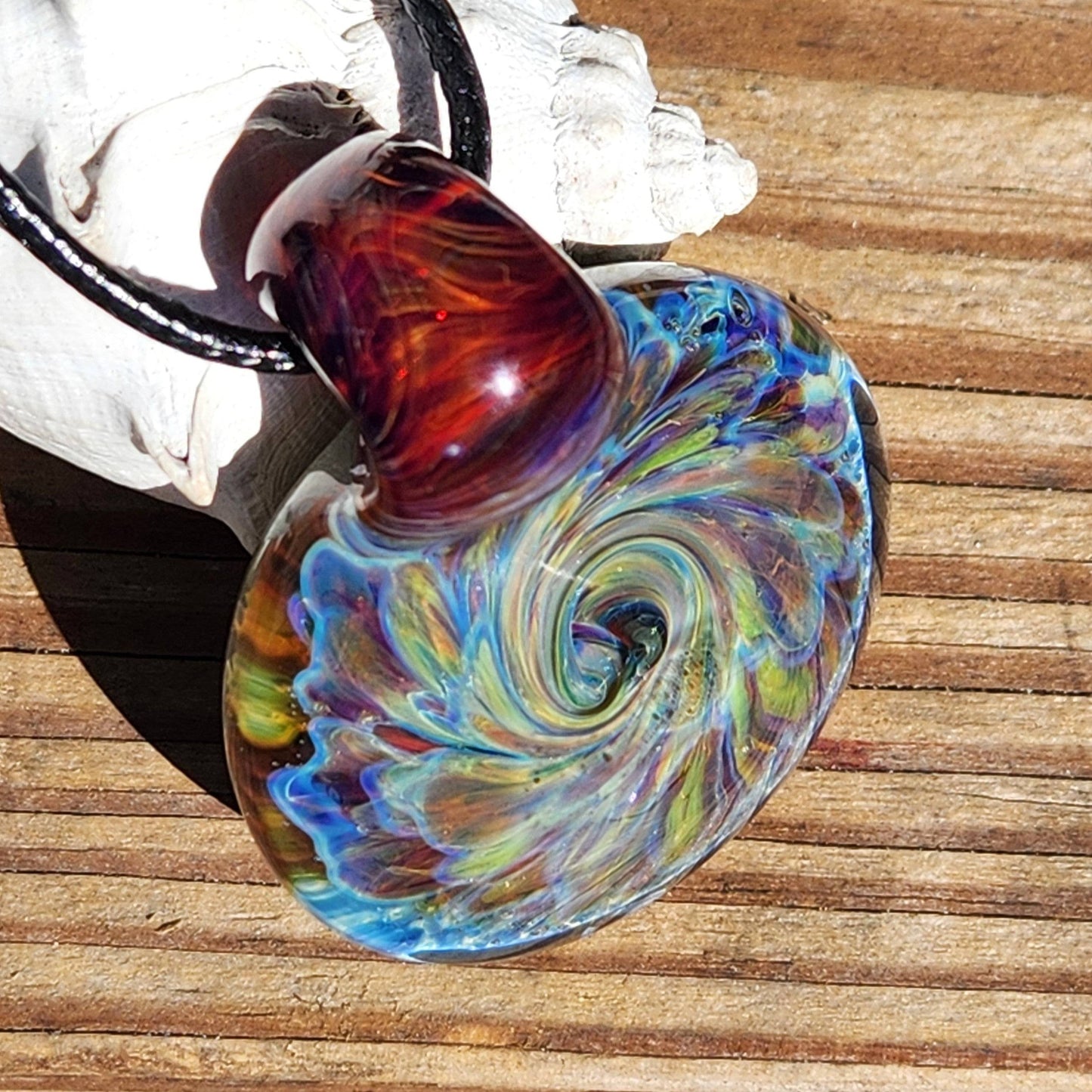 Handmade glass pendant with vibrant swirl design in blue, purple, and red tones, displayed on wood background.
