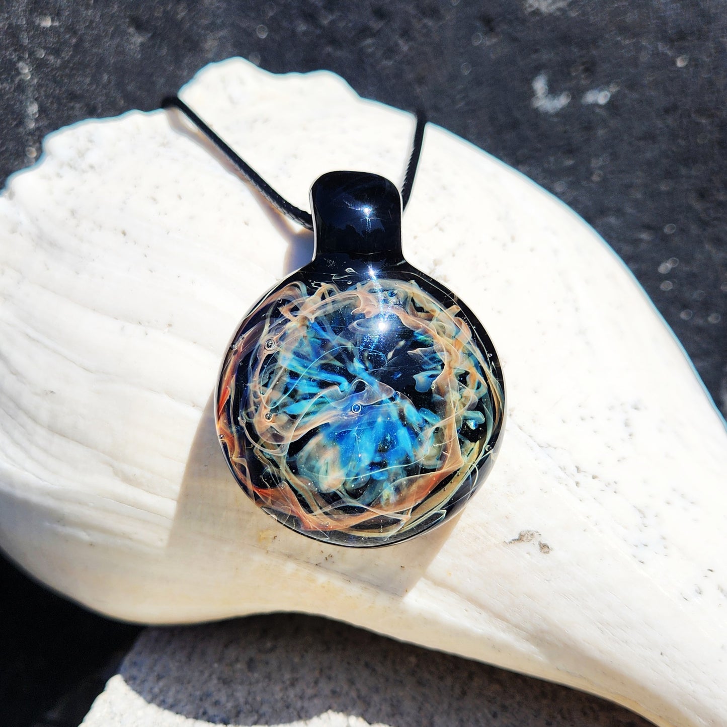 Necklace with a round pendant featuring a blue and orange design, placed on a white shell.