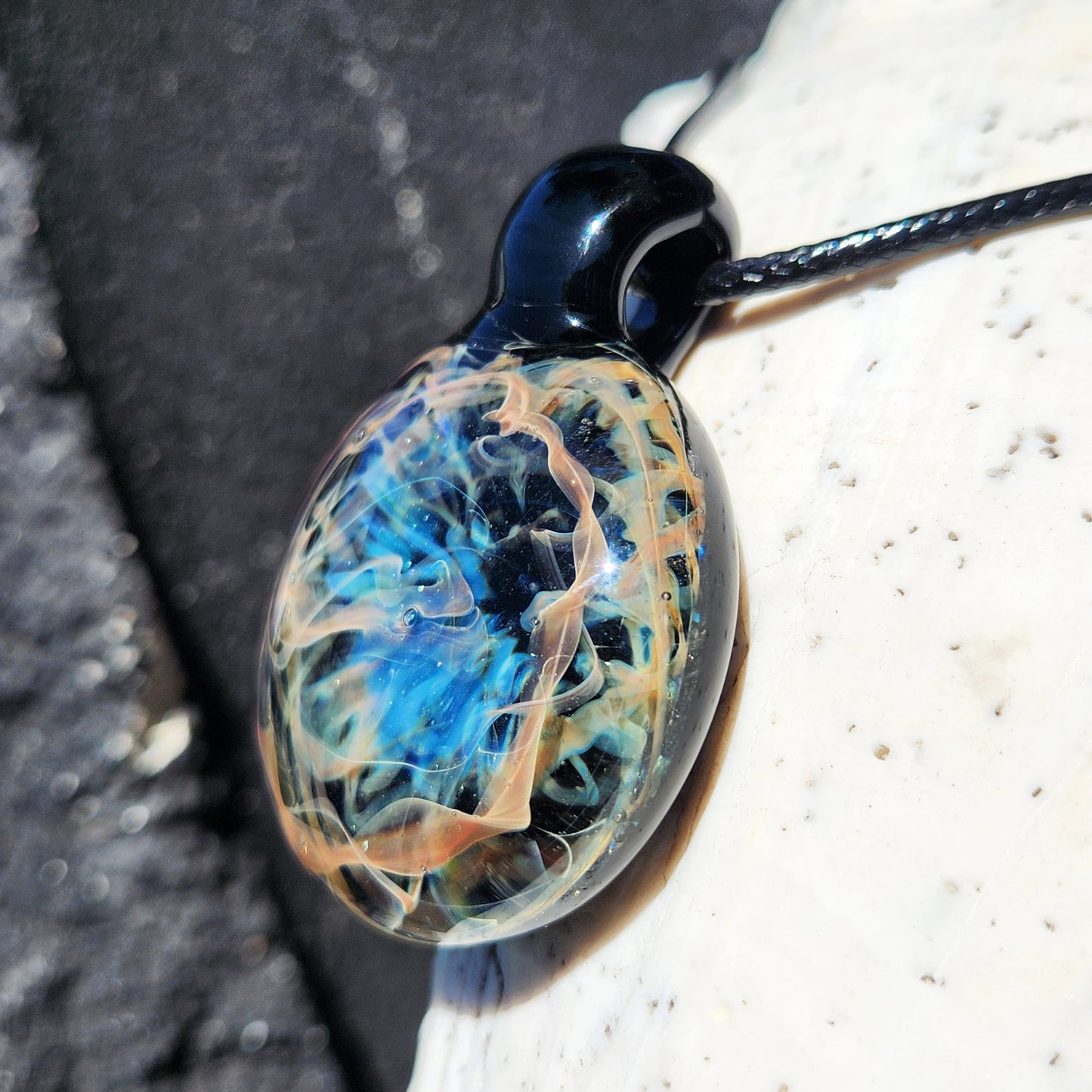 Glass pendant with blue and orange swirls on a dark background