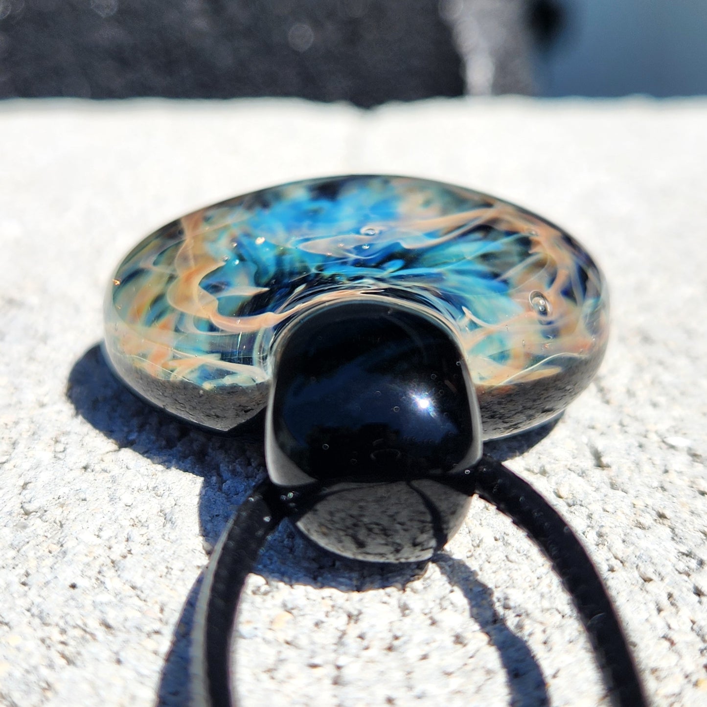 Glass pendant necklace with blue and black design on a textured surface