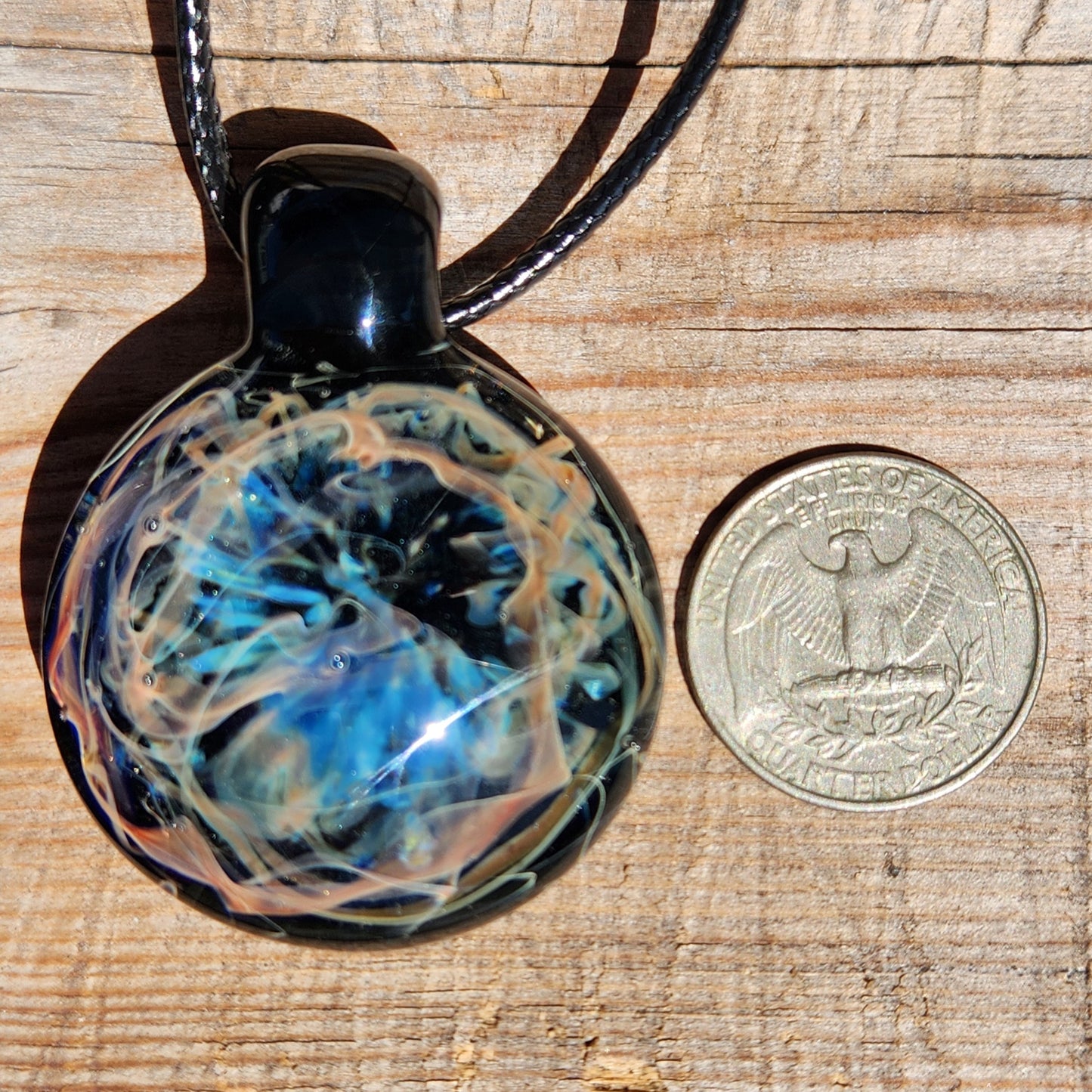 Glass pendant with blue and black marbled design next to a coin on a wooden surface