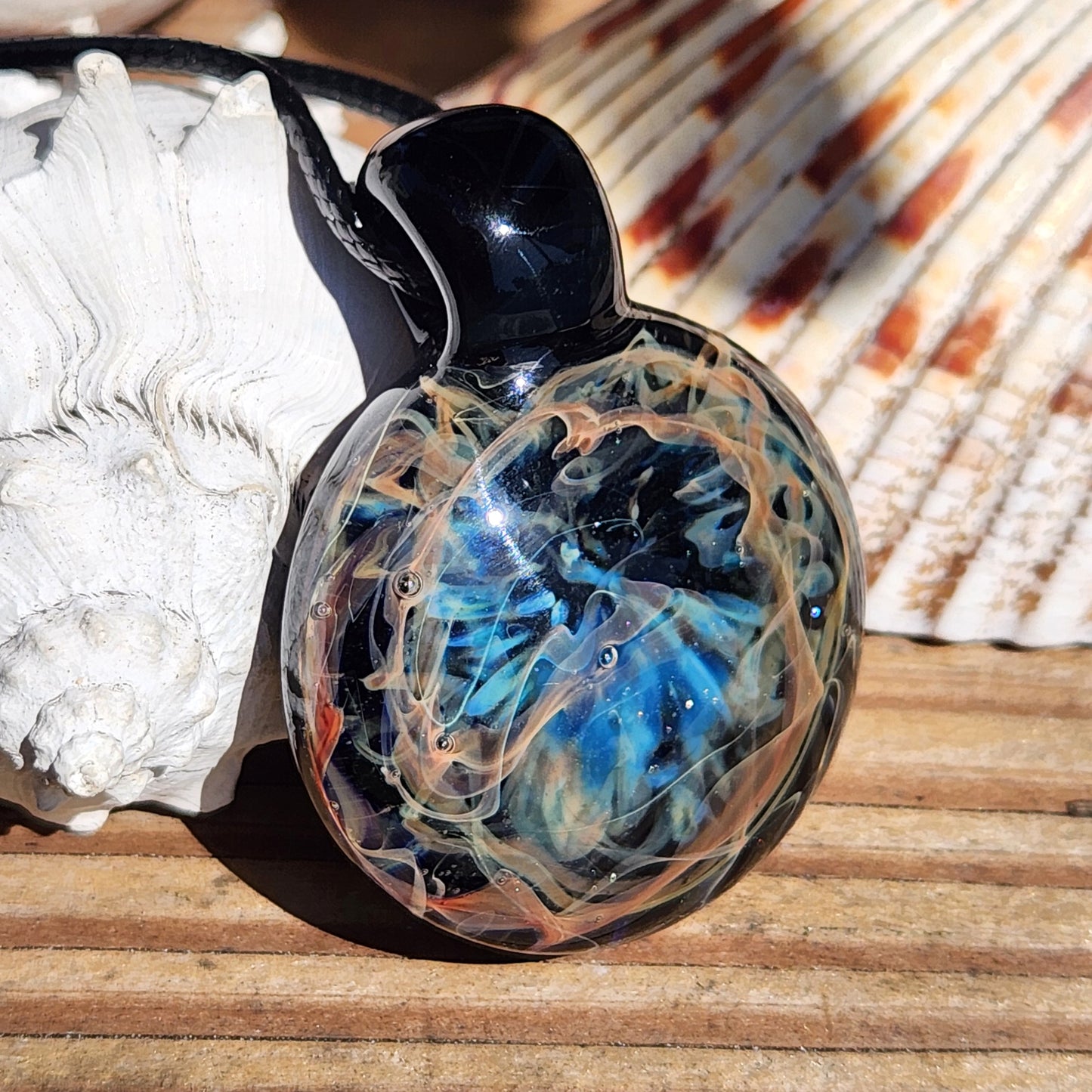 Glass pendant with marbled design on a wooden surface with shells in the background
