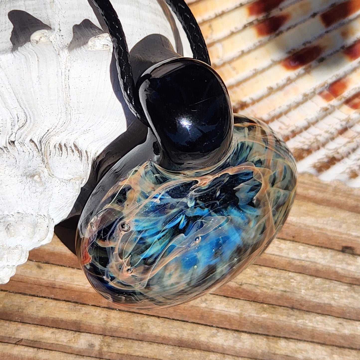 Glass pendant with black stone on a shell and wooden surface