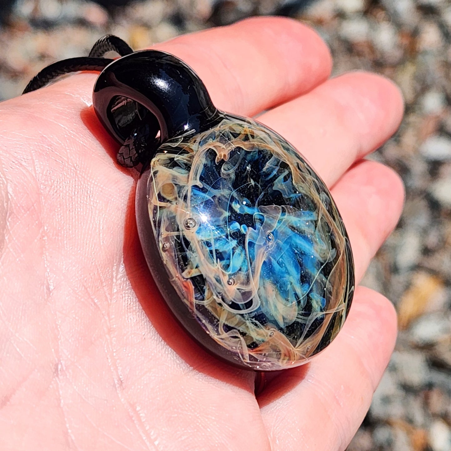 Handmade glass pendant held in a hand for size comparison with a blurred natural background