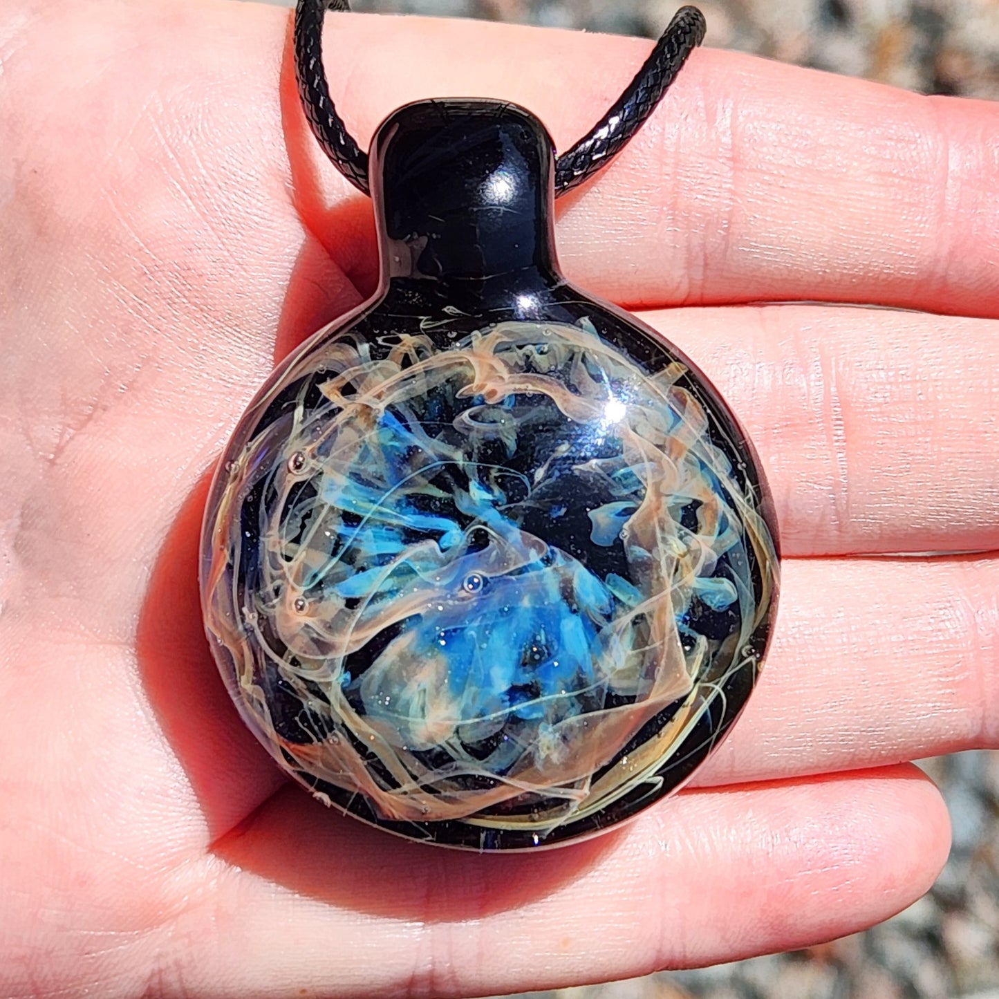 Round pendant with blue and beige design held in a hand