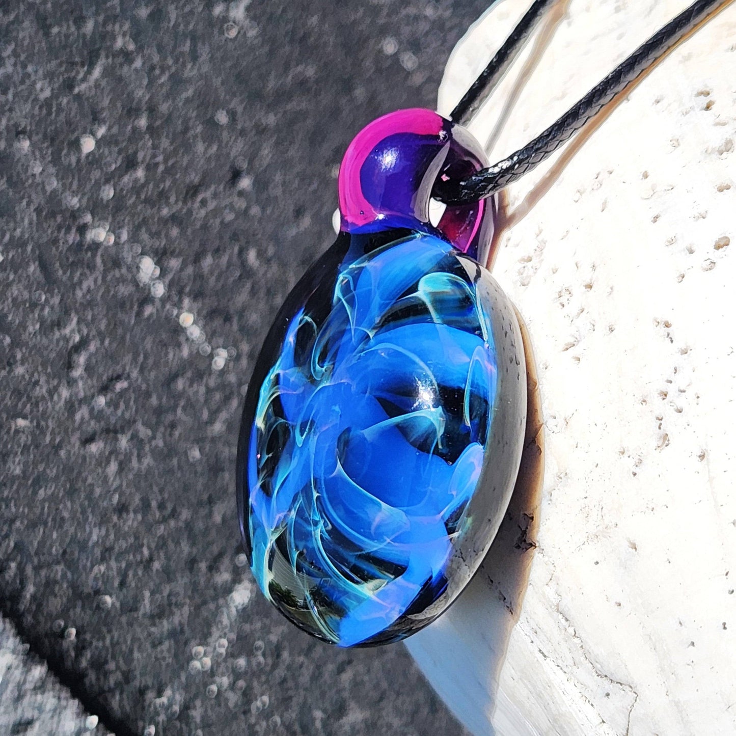 Angled view of Handmade Blue Swirl Glass Pendant Necklace with swirling blue patterns and translucent purple loop.