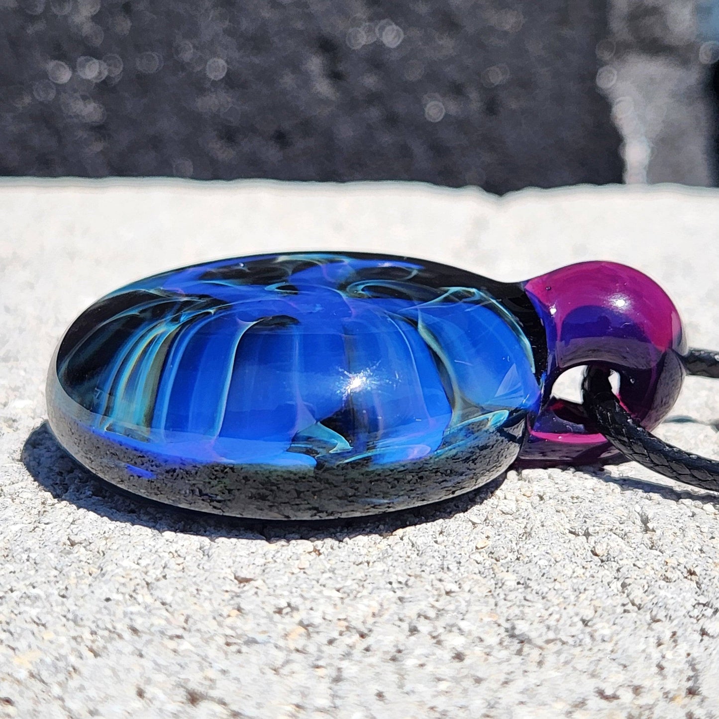 Low angle of Handmade Blue Swirl Glass Pendant Necklace emphasizing the glossy black base and vivid blue swirls.