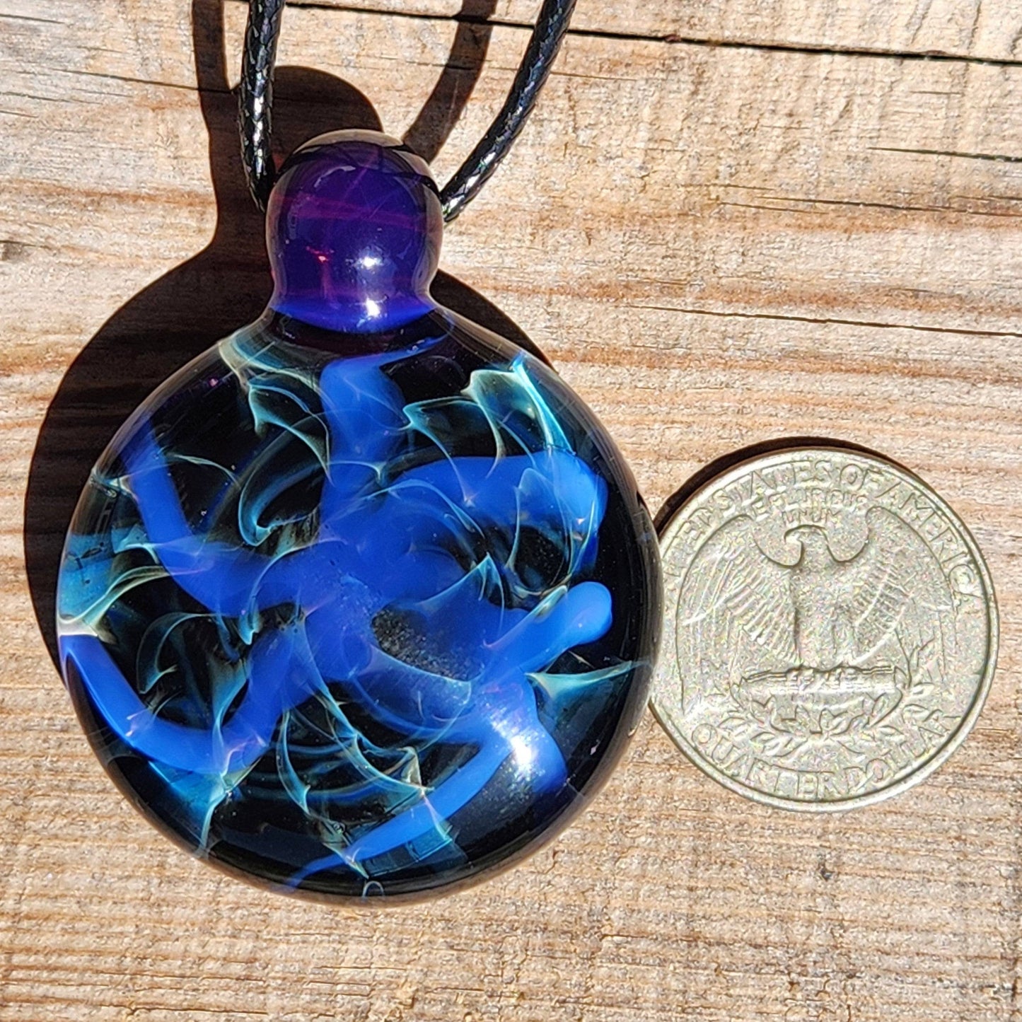 Handmade Blue Swirl Glass Pendant Necklace next to a US quarter for size comparison, highlighting its compact design.