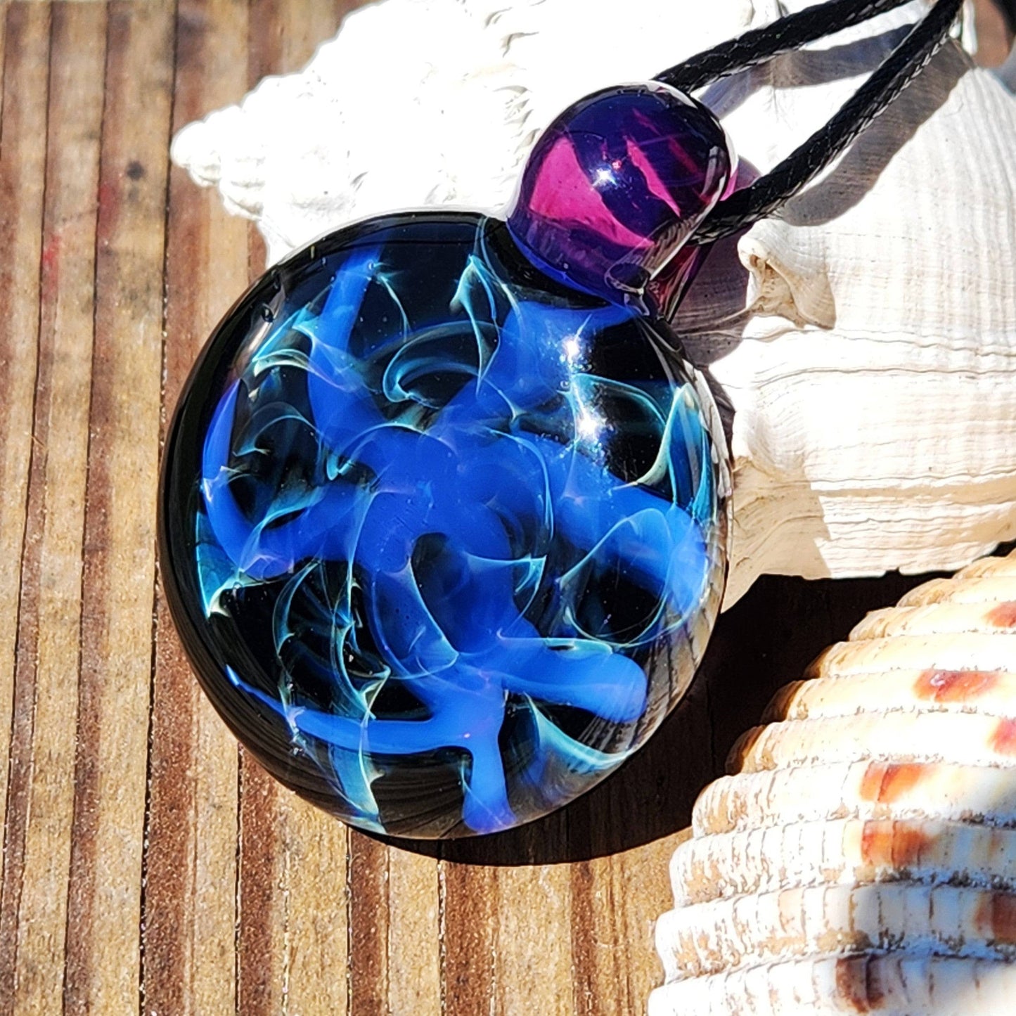 Handmade Blue Swirl Glass Pendant Necklace resting on wood with seashells, showcasing its vibrant blue and teal design.