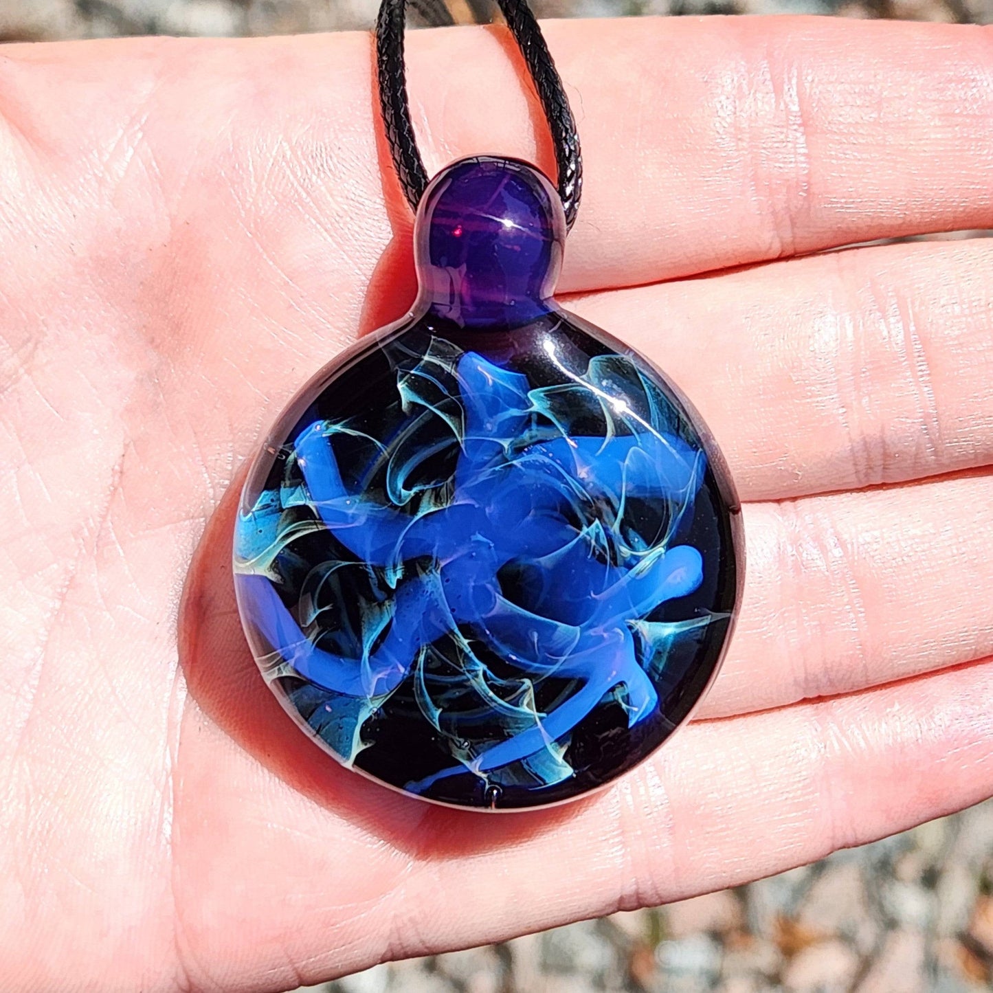 Handmade Blue Swirl Glass Pendant Necklace shown in palm for scale, featuring vivid blue swirls and a purple loop.