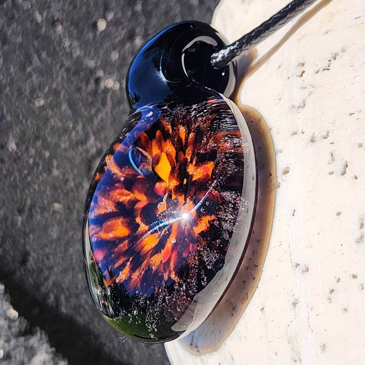 Angled view of Fiery Glass Pendant Necklace with intense orange and red fire bloom inside clear glass, handmade fall accessory.