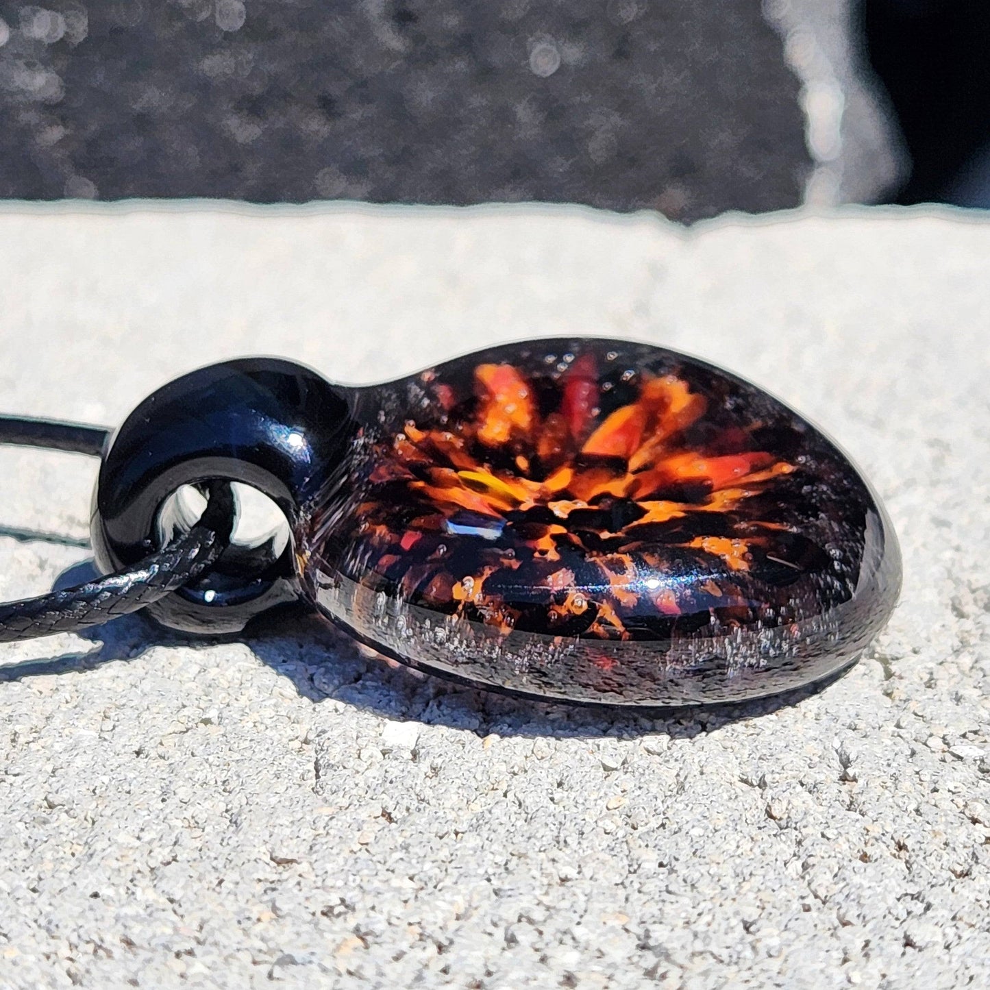 Fiery Glass Pendant with swirling red and orange bloom on black background, unique handmade Halloween necklace for seasonal wear.