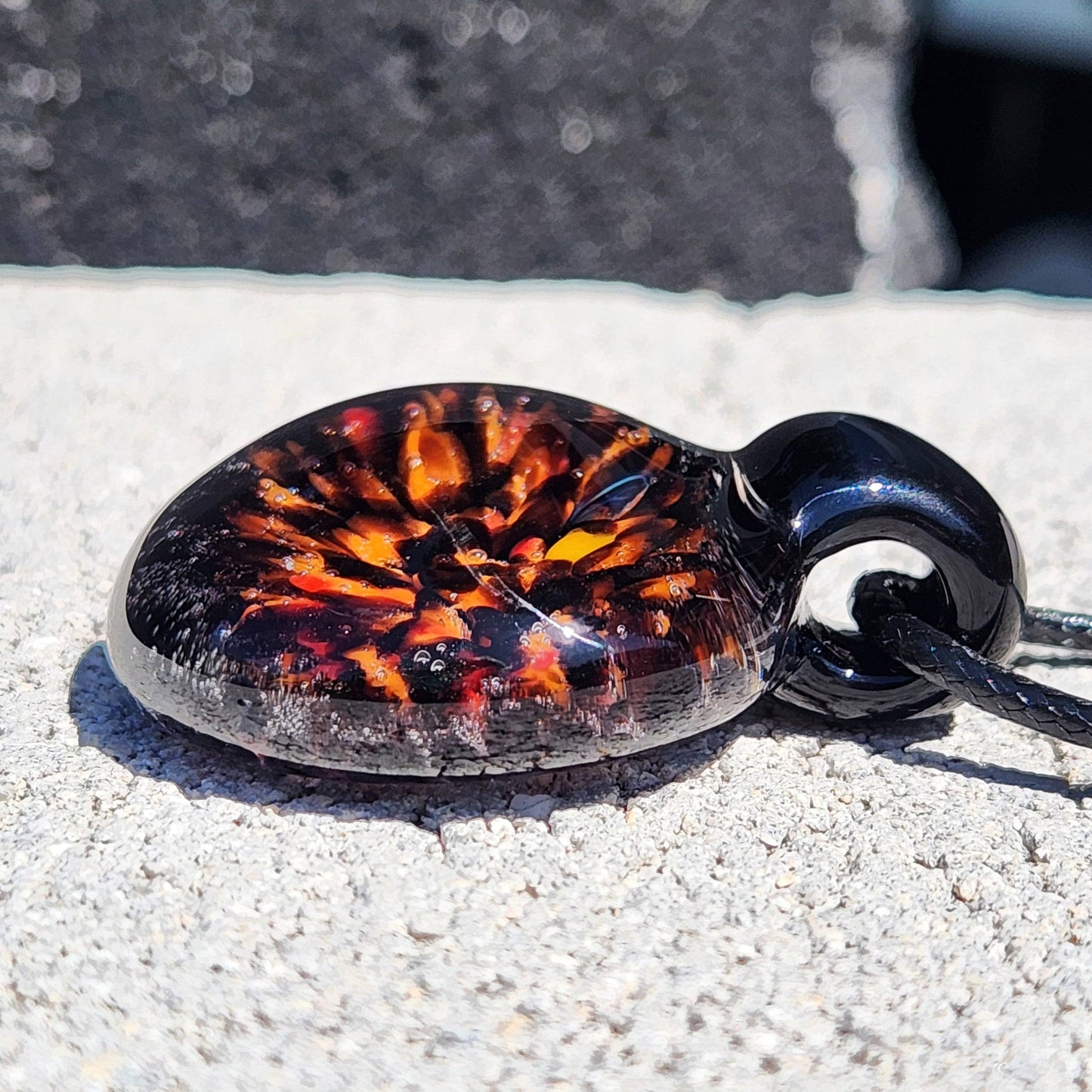 Close-up of handmade Fiery Glass Pendant with glowing fire bloom design, black glass base and smooth finish, ideal Halloween accessory.