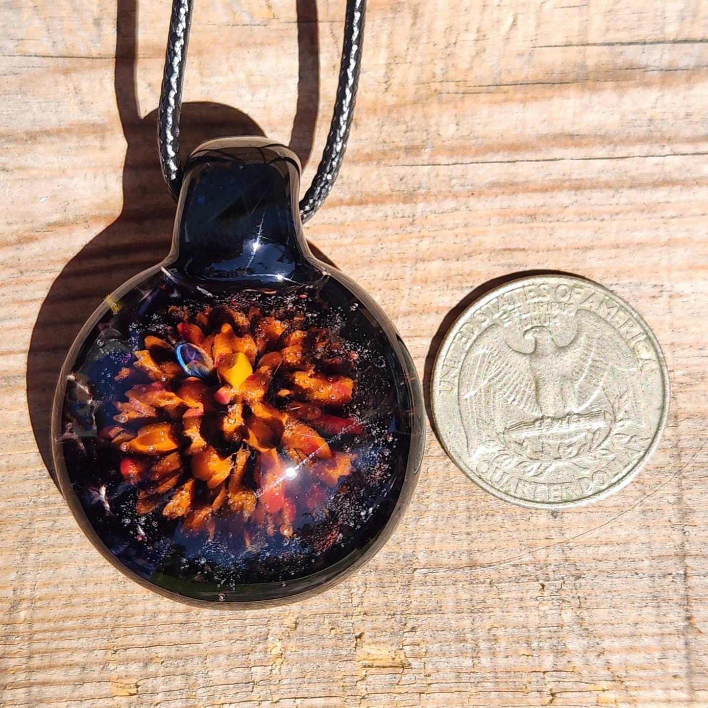 Fiery Glass Pendant Necklace shown next to a US quarter for size comparison, handmade Halloween jewelry with vibrant flame design.