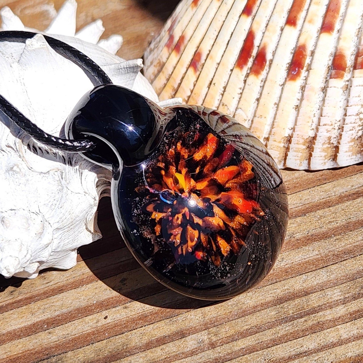 Fiery Glass Pendant Necklace resting on seashells, showcasing vibrant orange-red bloom and black glass, unique handmade Halloween jewelry.