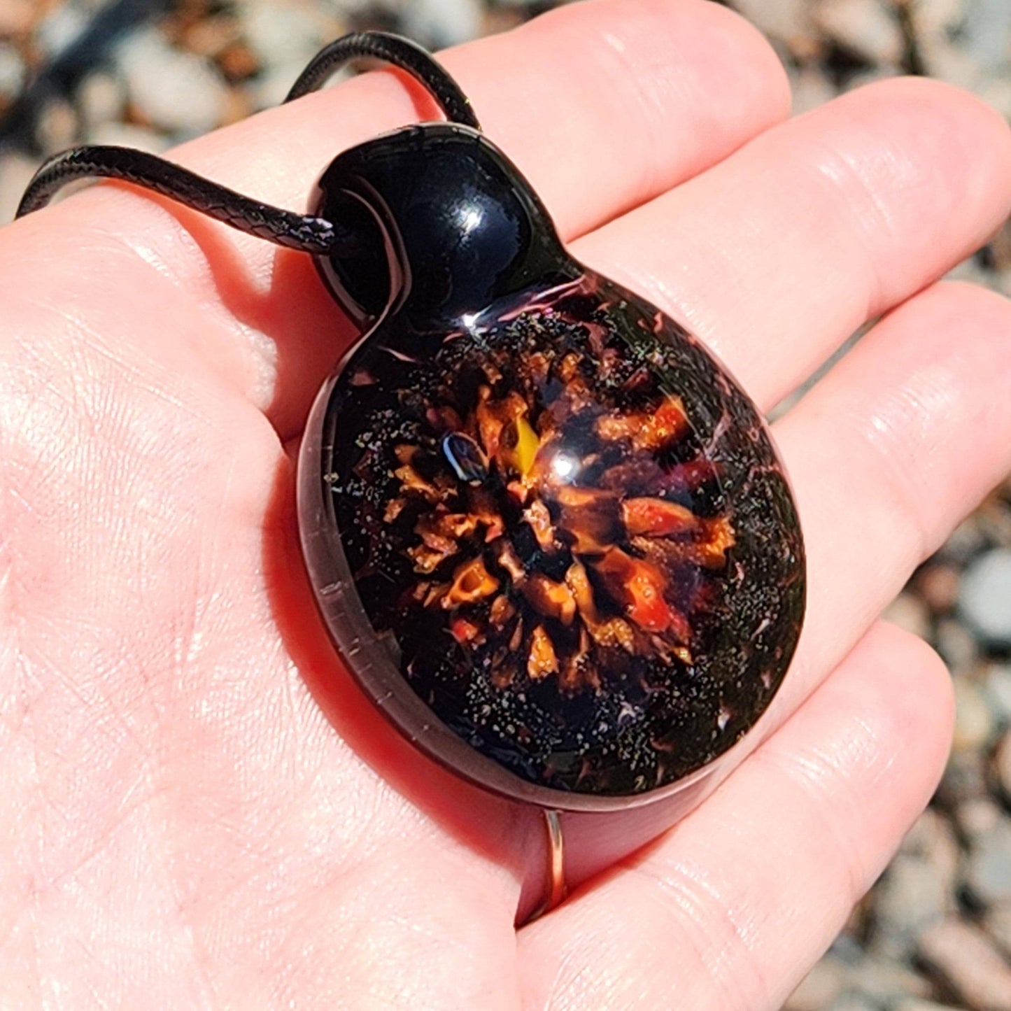 Fiery Glass Pendant resting in hand, showcasing detailed orange and red fire bloom, handmade Halloween-inspired blown glass jewelry.