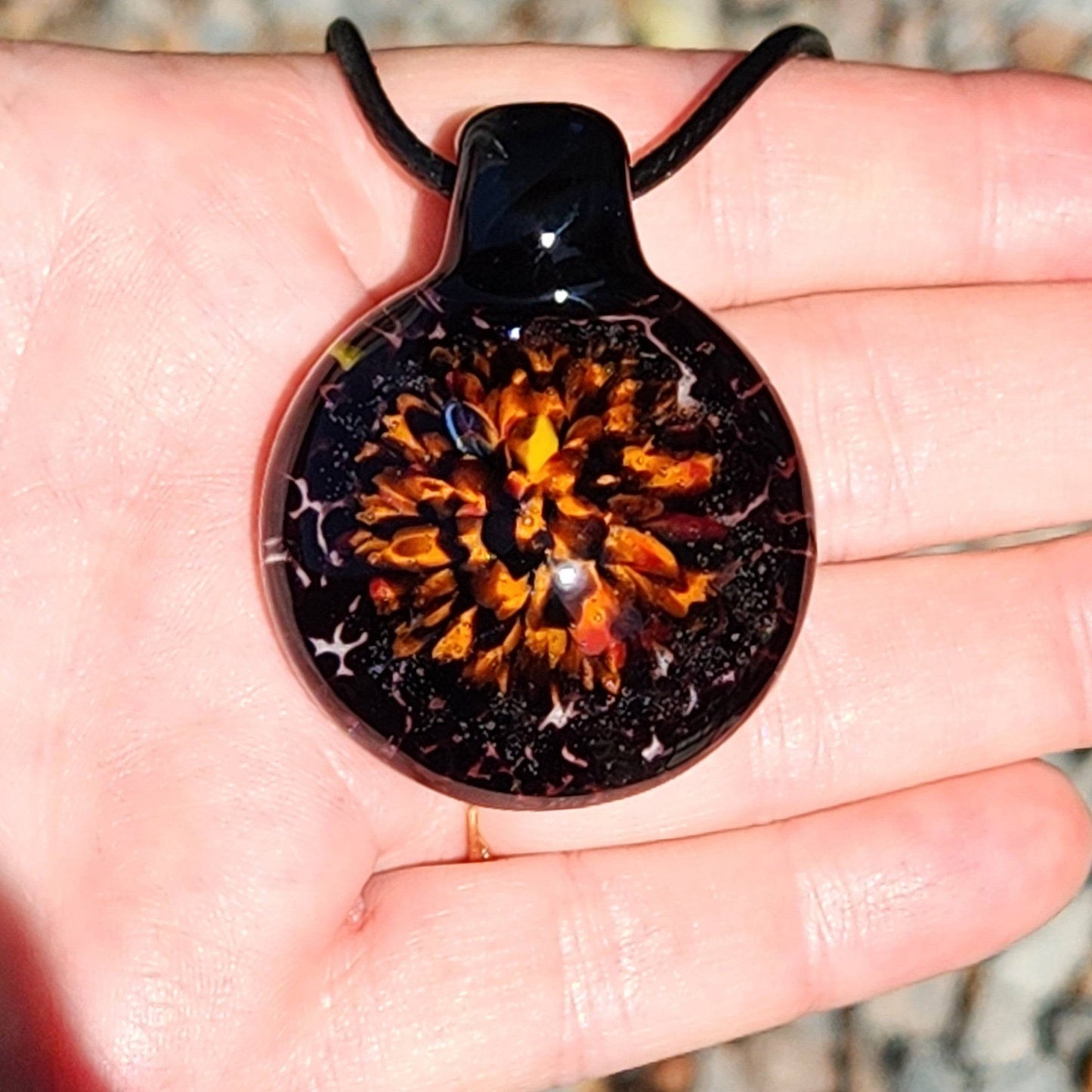Front view of Fiery Glass Pendant Necklace in hand, featuring vivid flame-like bloom and black glass, perfect handmade fall gift.