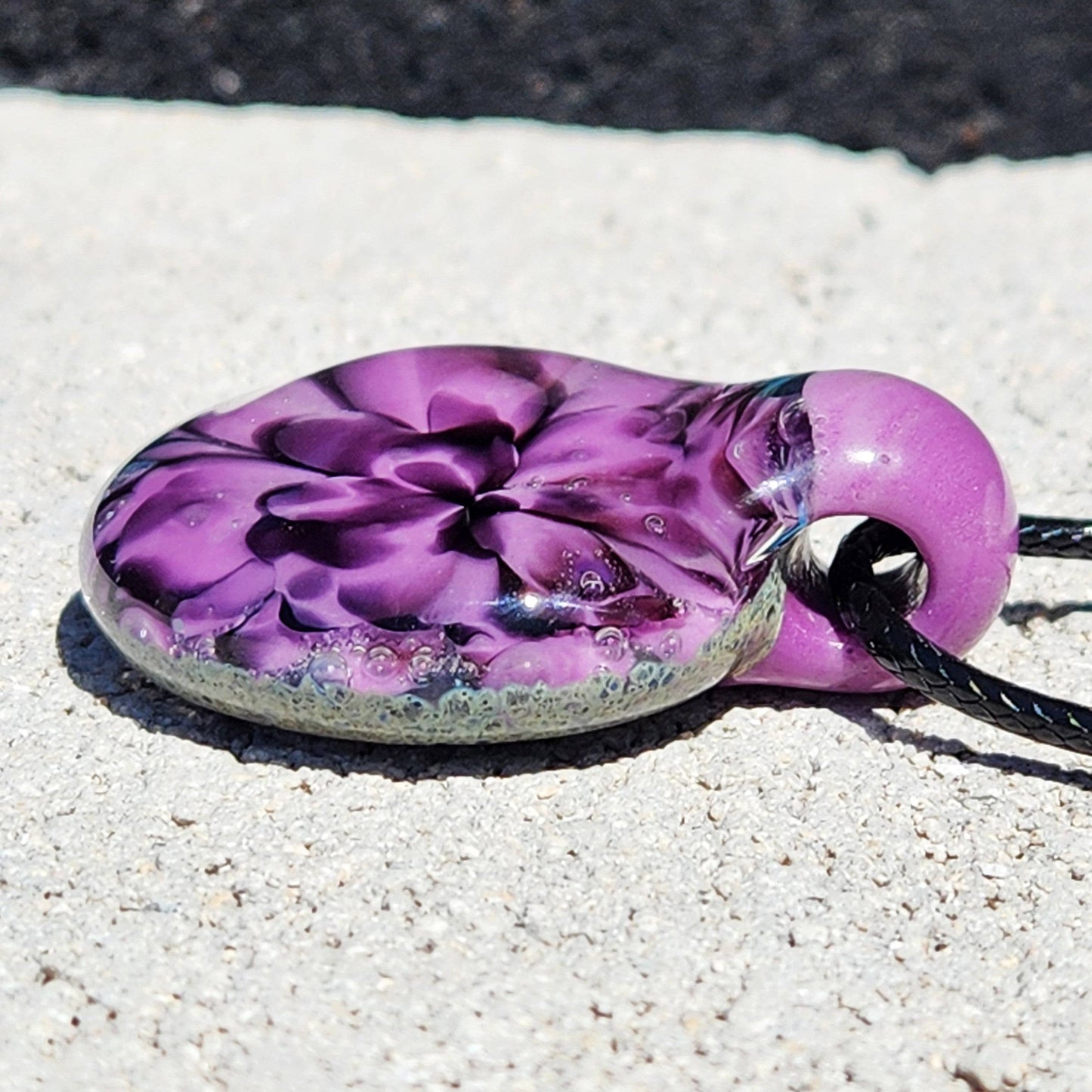 Flat-lay of purple floral pendant necklace with black cord, highlighting the detailed glasswork and color gradient. Unique handmade charm.